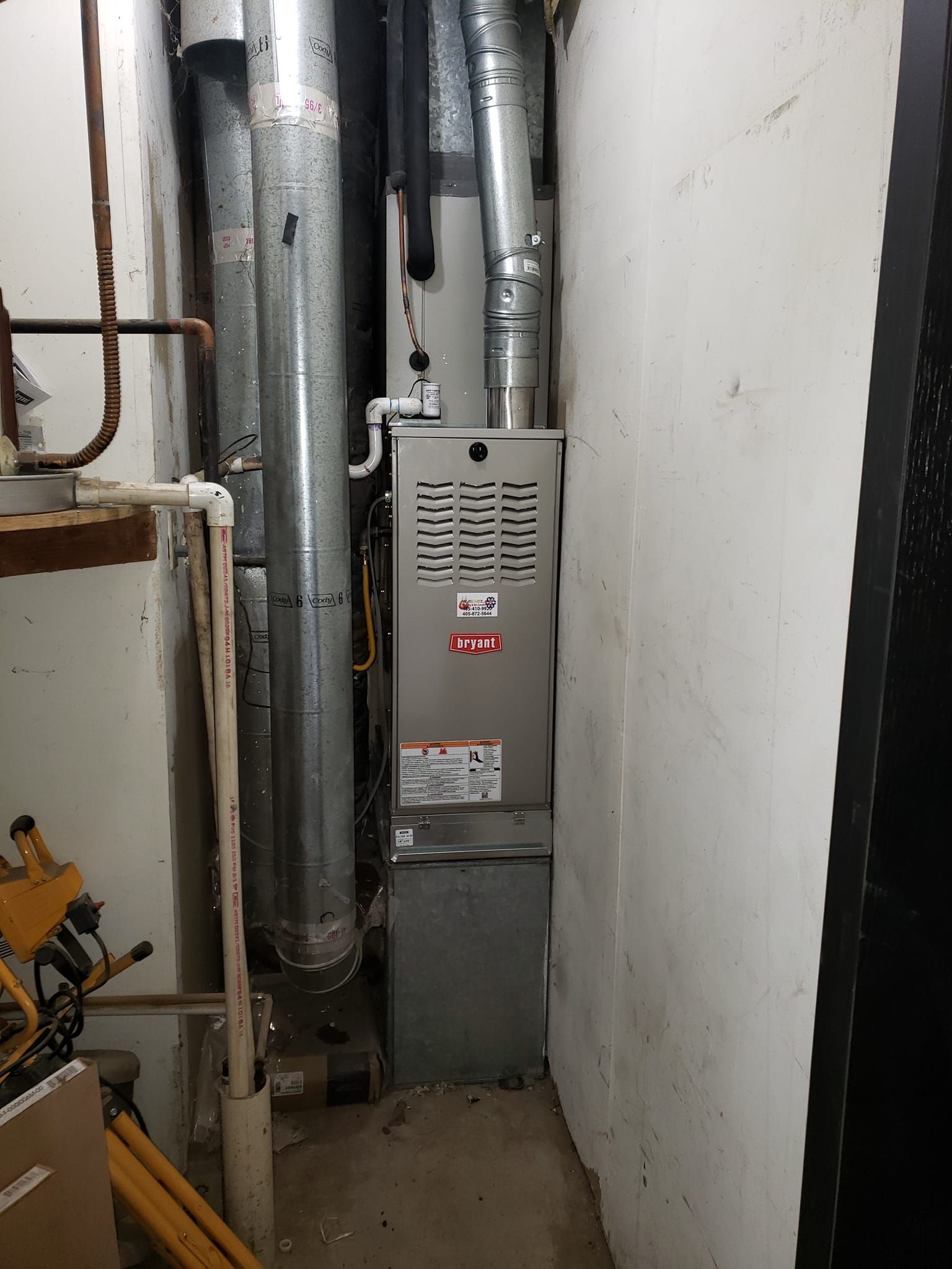 A furnace is sitting in a narrow room next to a wall.