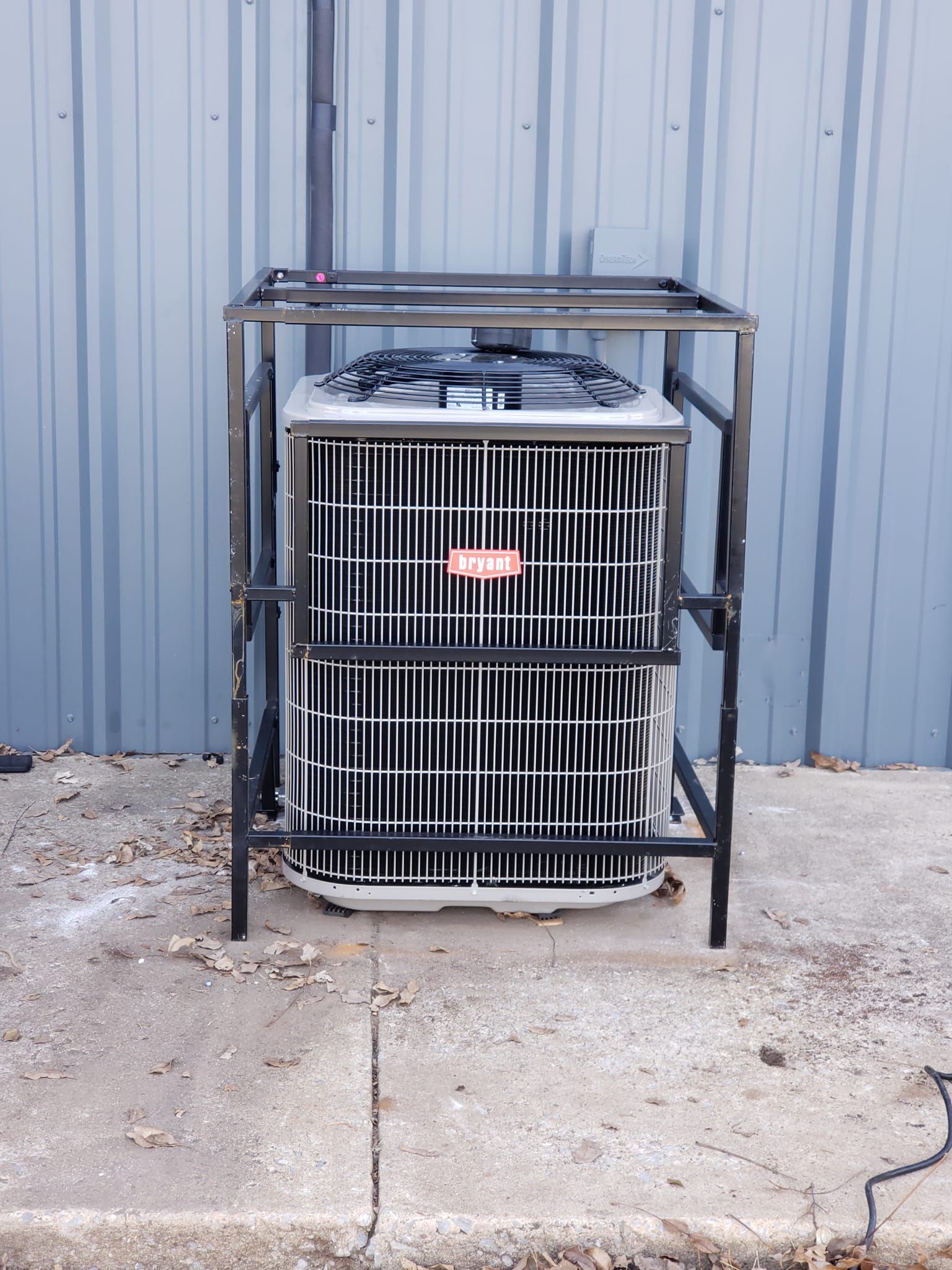 An air conditioner is sitting in a metal cage on the sidewalk.