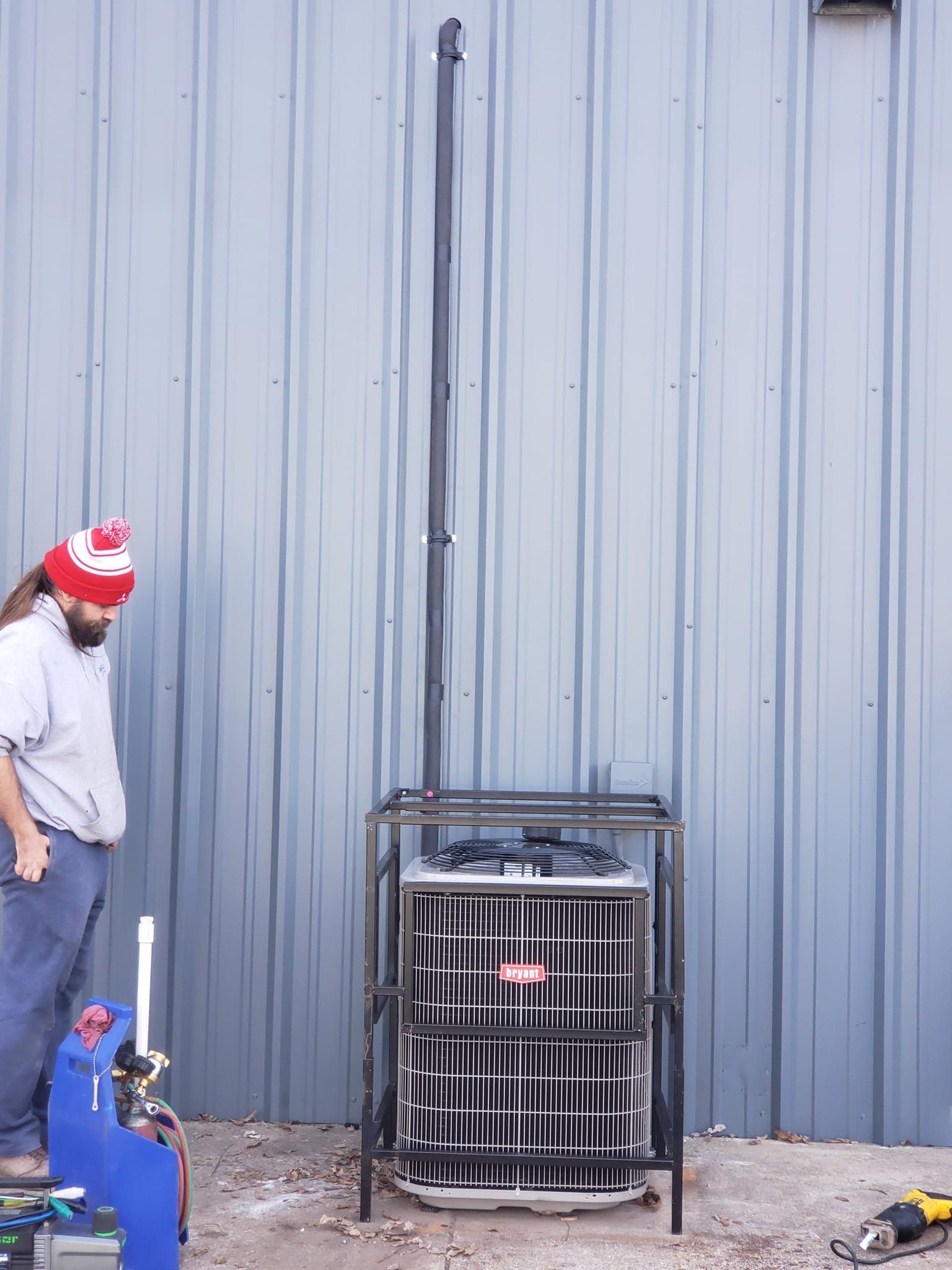 A man in a red and white hat is working on an air conditioner outside of a building.