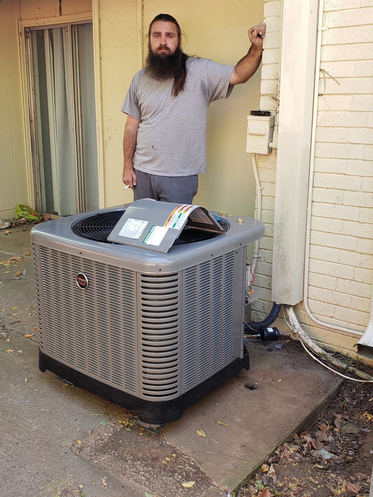 A man with a beard is standing next to an air conditioner.