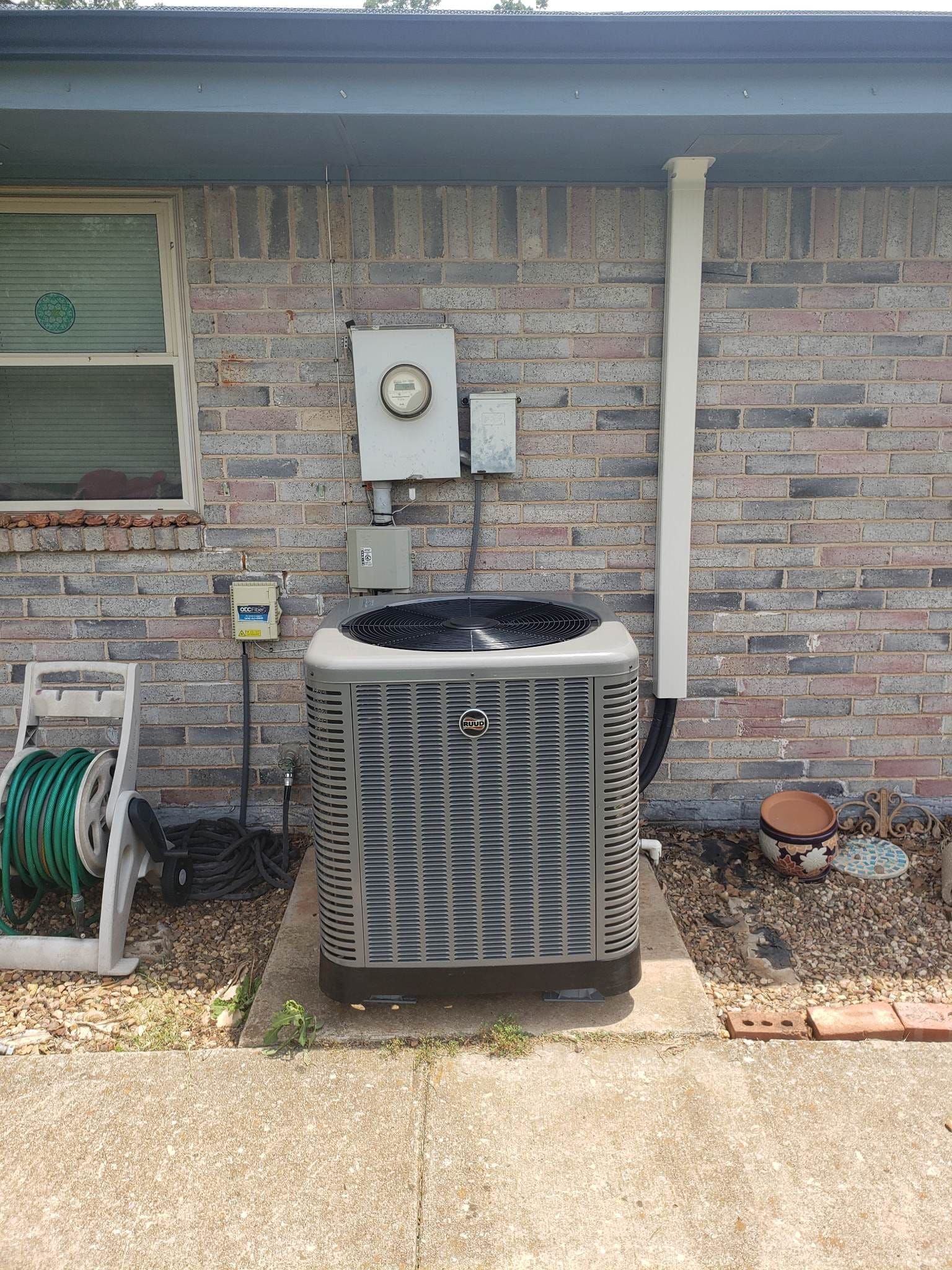 An air conditioner is sitting on the side of a brick house.