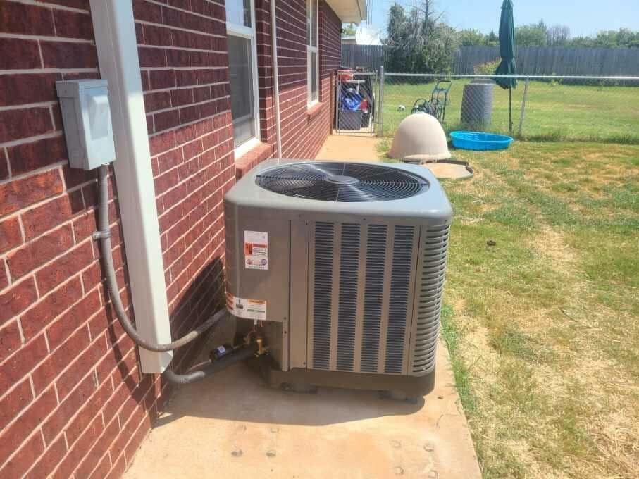 An air conditioner is sitting on the side of a brick house.
