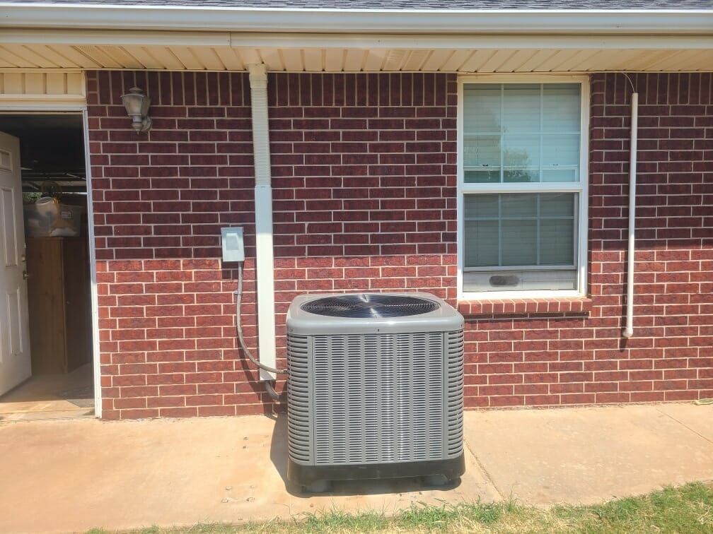 An air conditioner is sitting outside of a brick house next to a window.