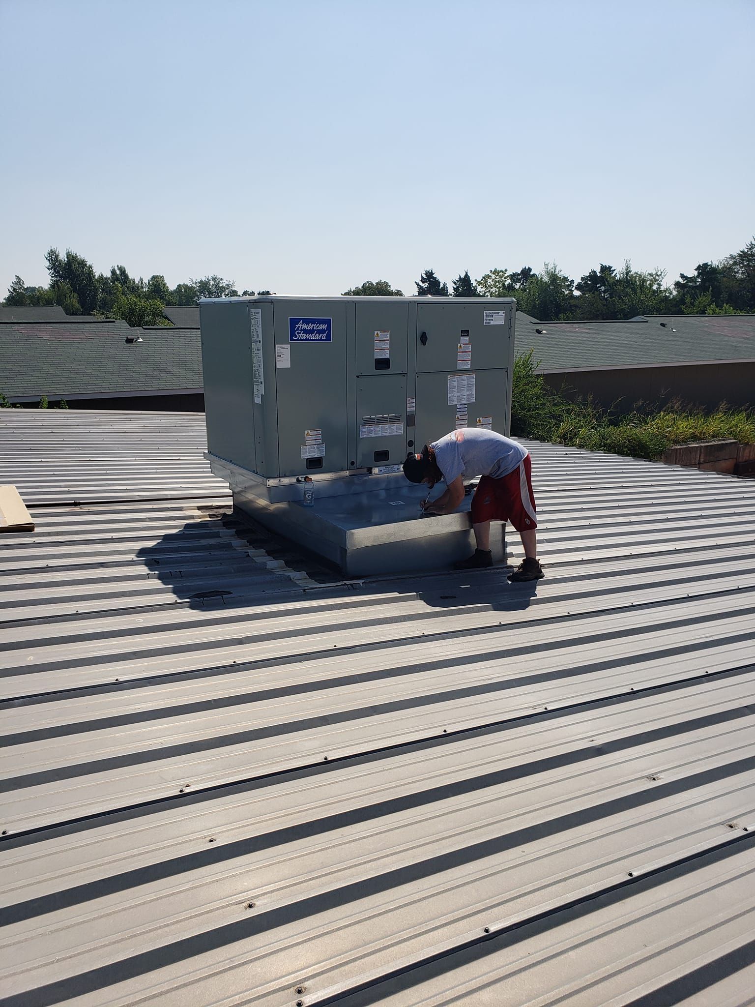 A man is working on an air conditioner on the roof of a building.