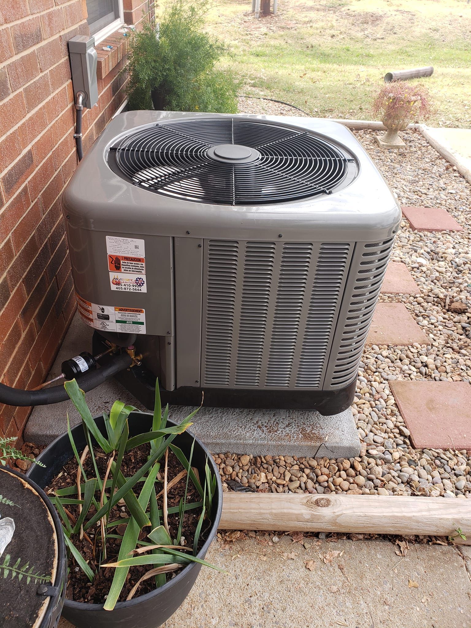 An air conditioner is sitting on the side of a brick building next to a potted plant.