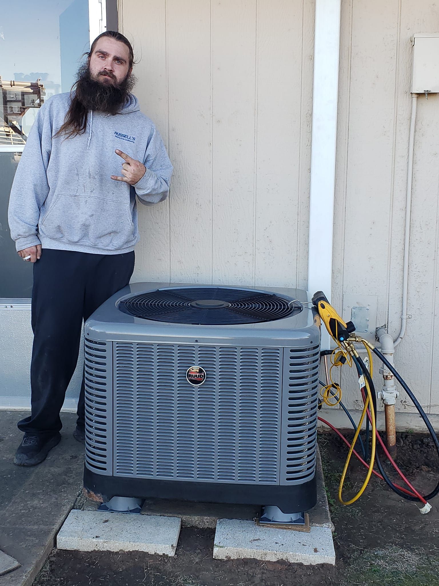 A man with a beard is standing next to an air conditioner.
