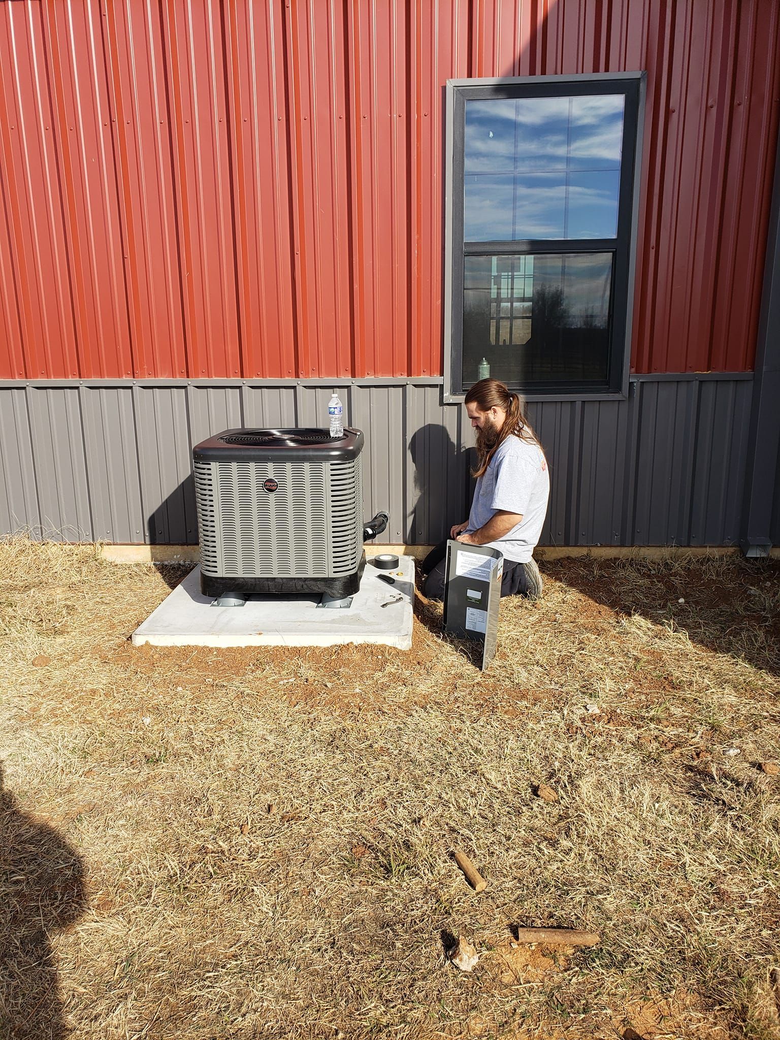 A man is sitting on a stool in front of a building next to an air conditioner.