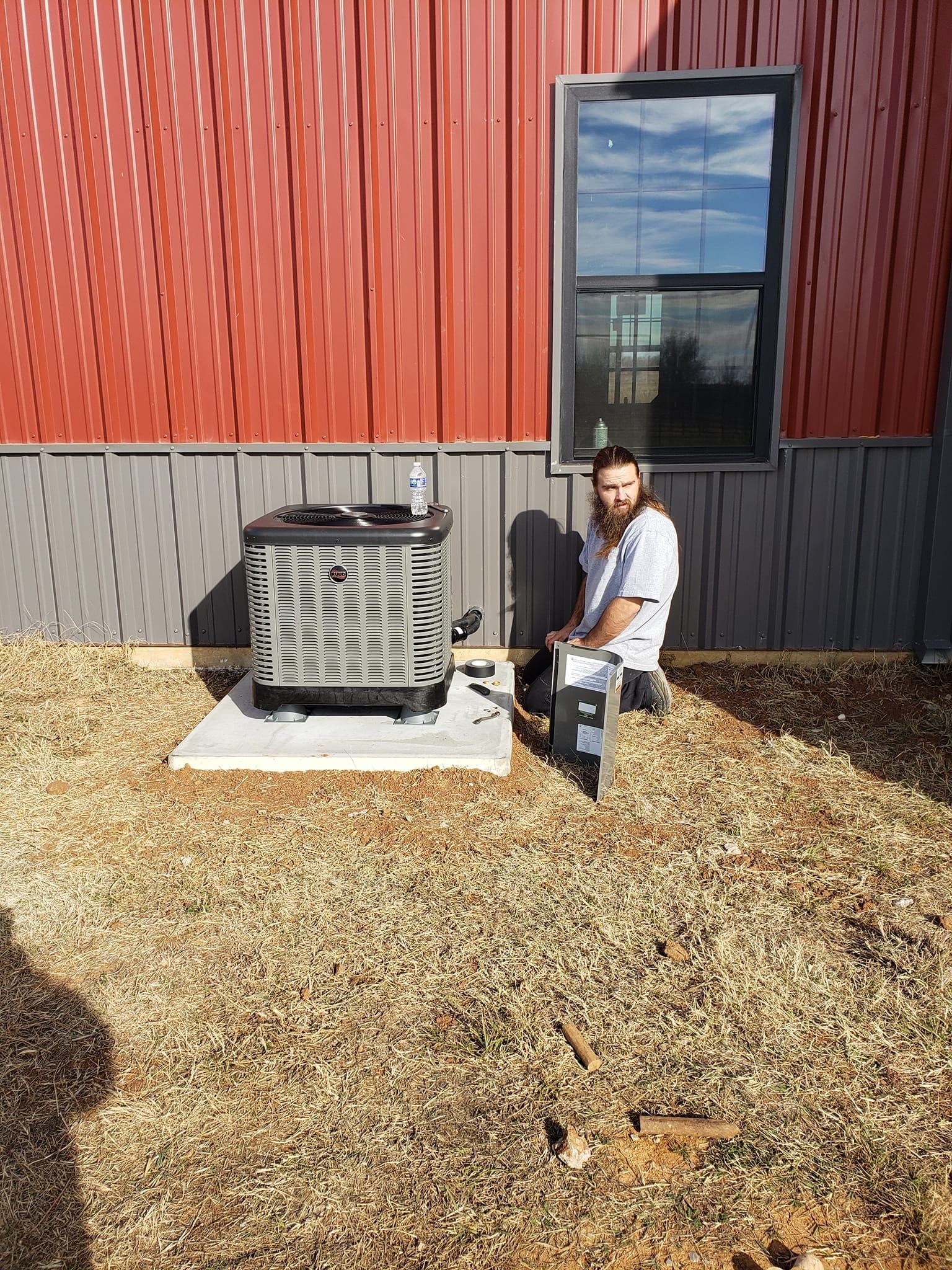 A man is sitting on a stool in front of a building next to an air conditioner.