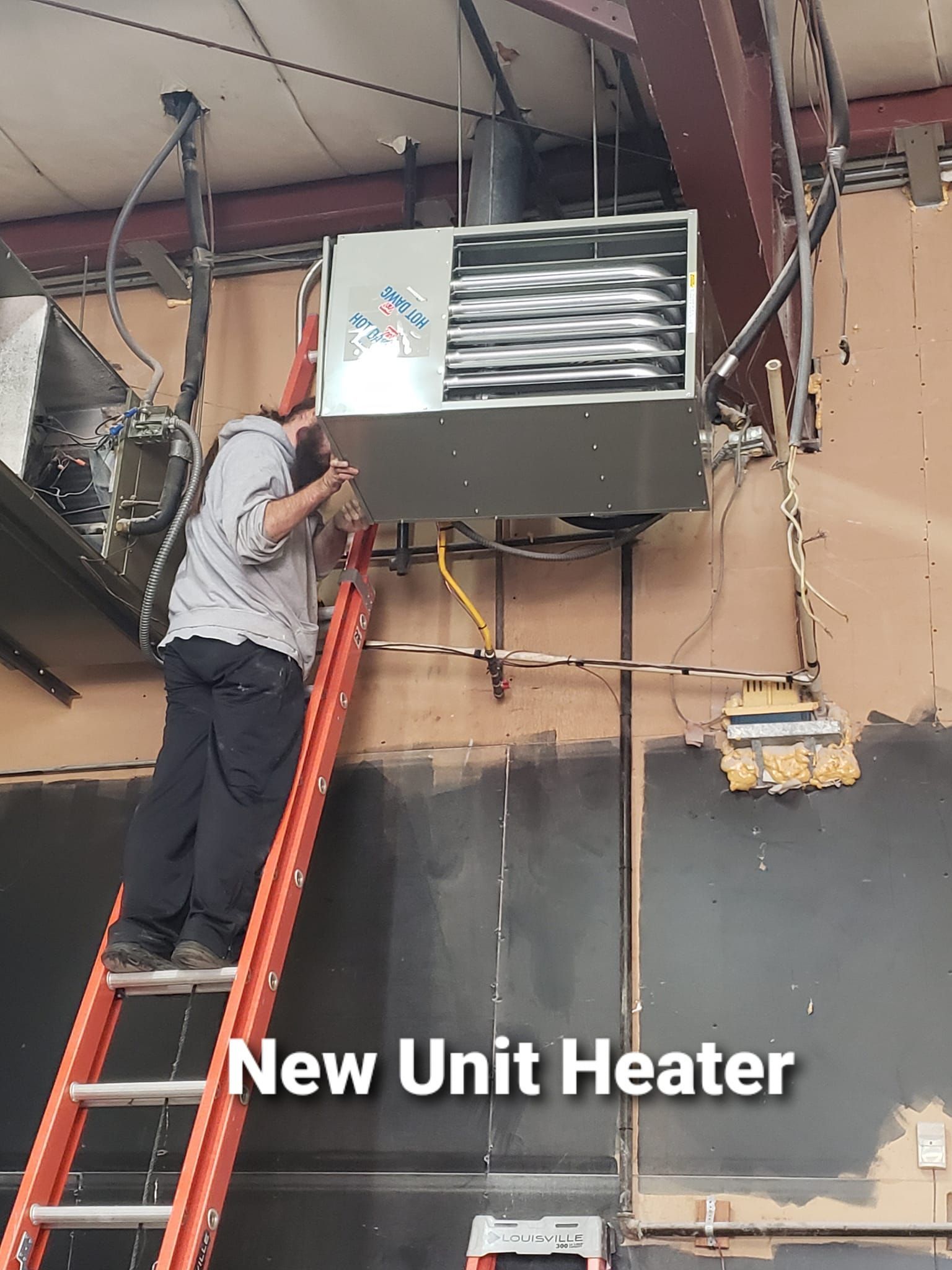 A man on a ladder working on a new unit heater