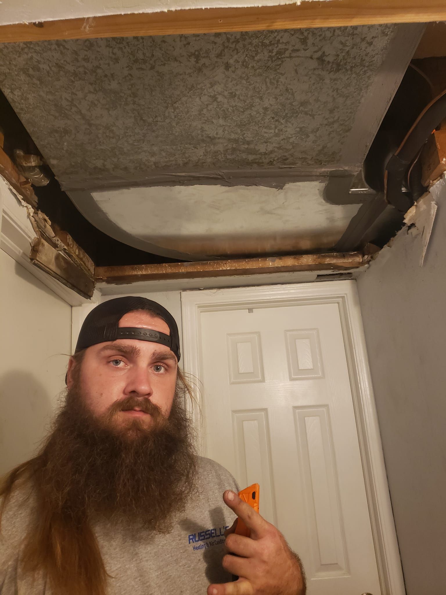A man with a beard is standing in a room holding a spray bottle.