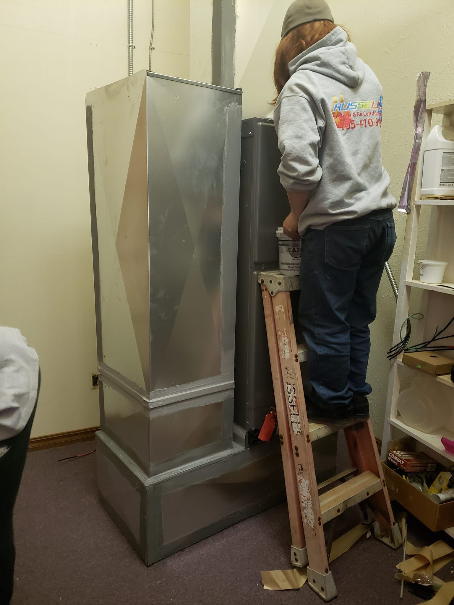 A man is standing on a ladder in front of a heater.