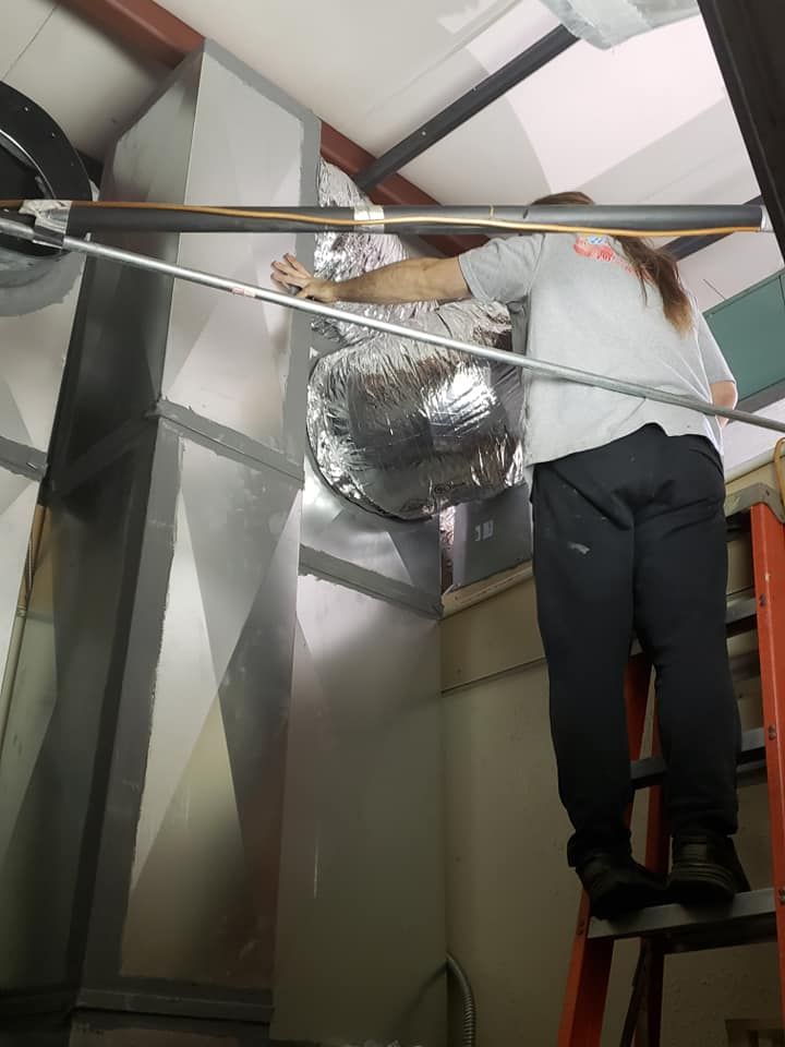 A woman is standing on a ladder holding a metal pole.