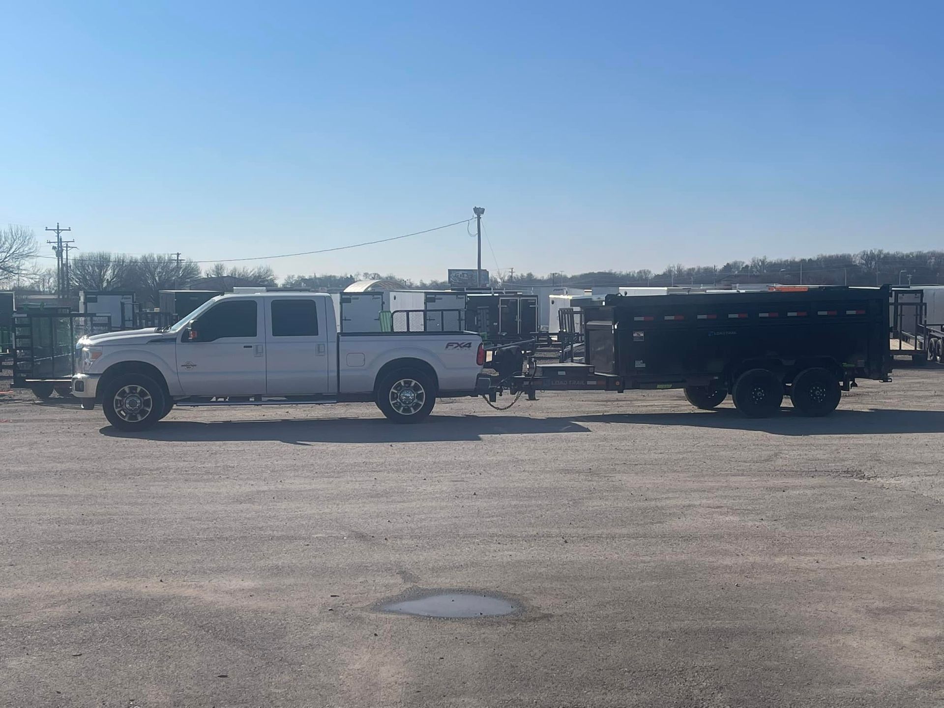 A white truck is pulling a trailer in a parking lot.