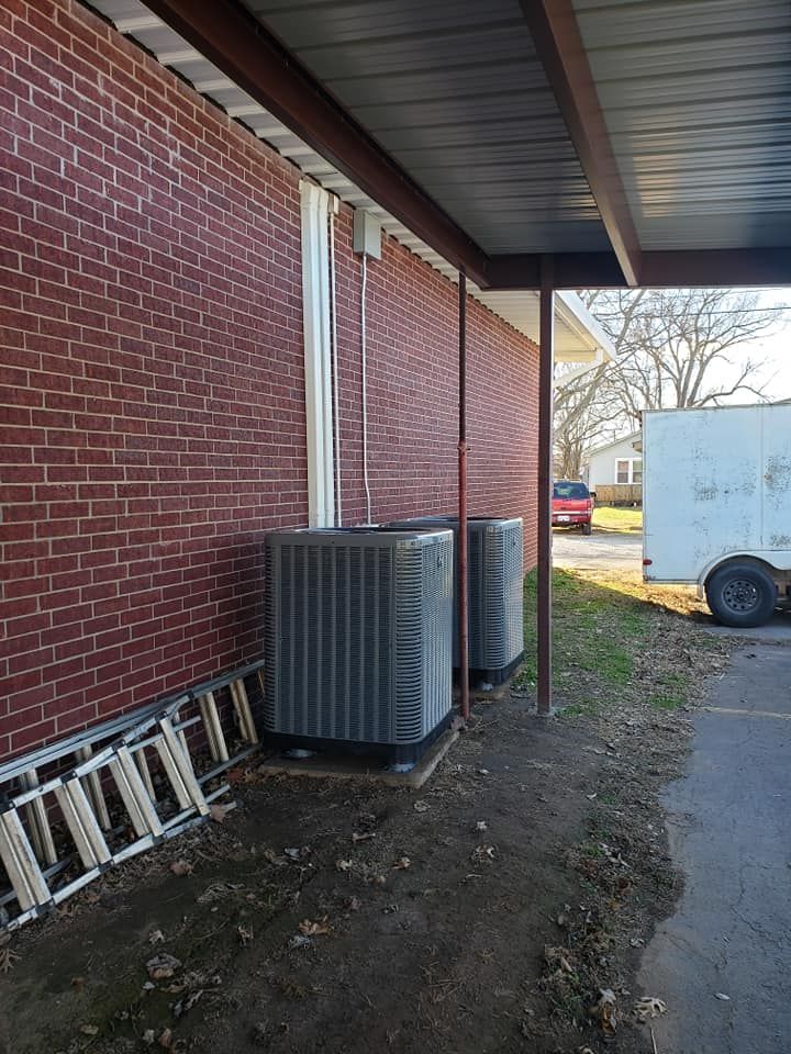 Two air conditioners are installed on the side of a brick building.