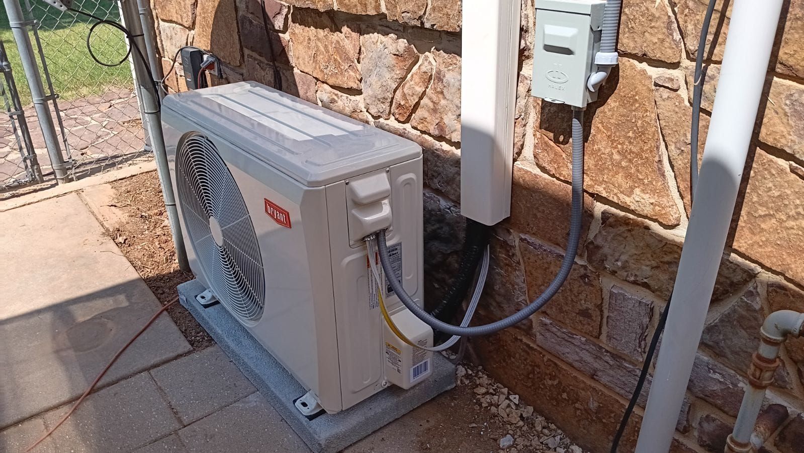 A white air conditioner is sitting on the side of a brick wall.