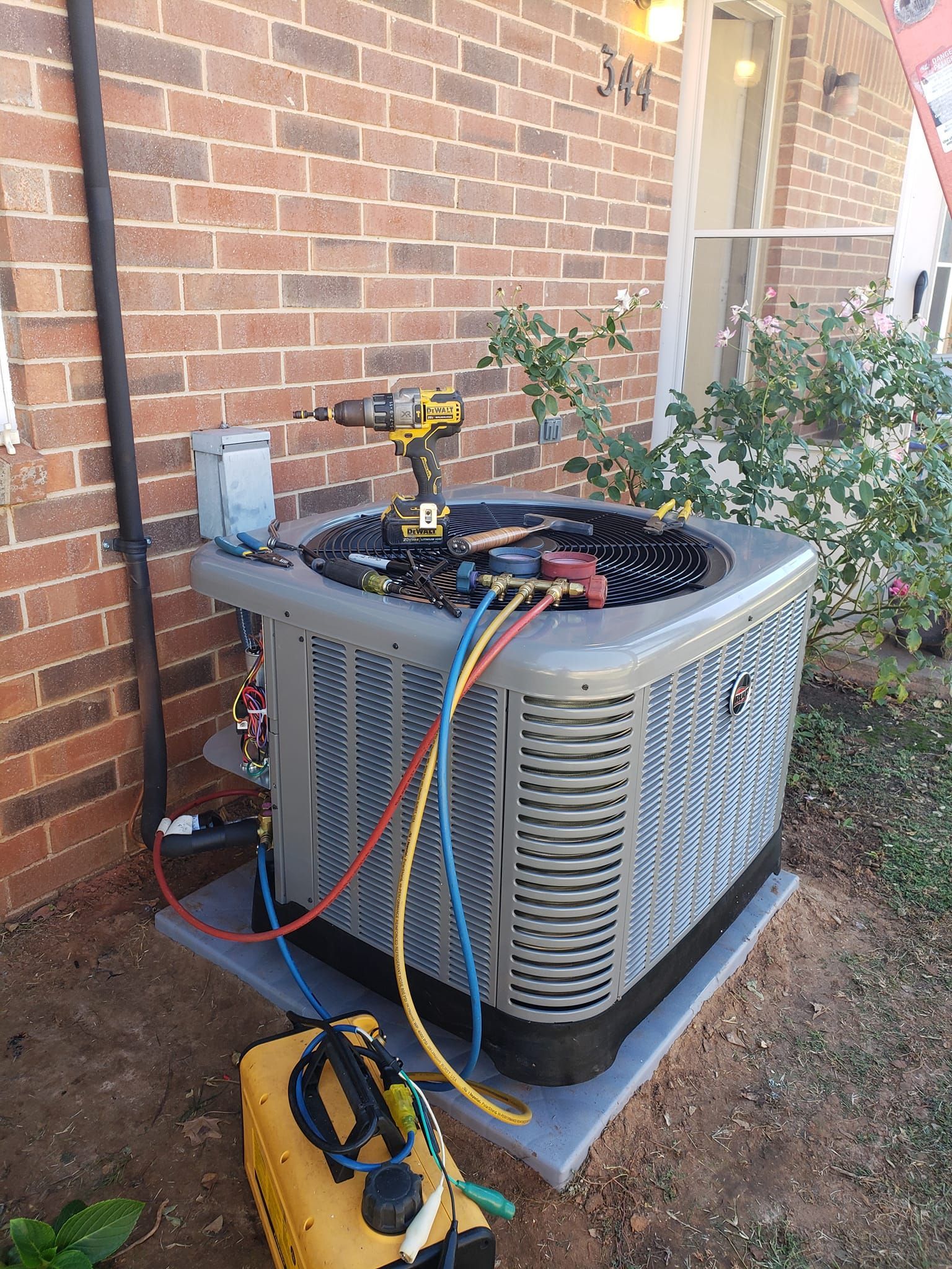An air conditioner is being repaired outside of a brick building.