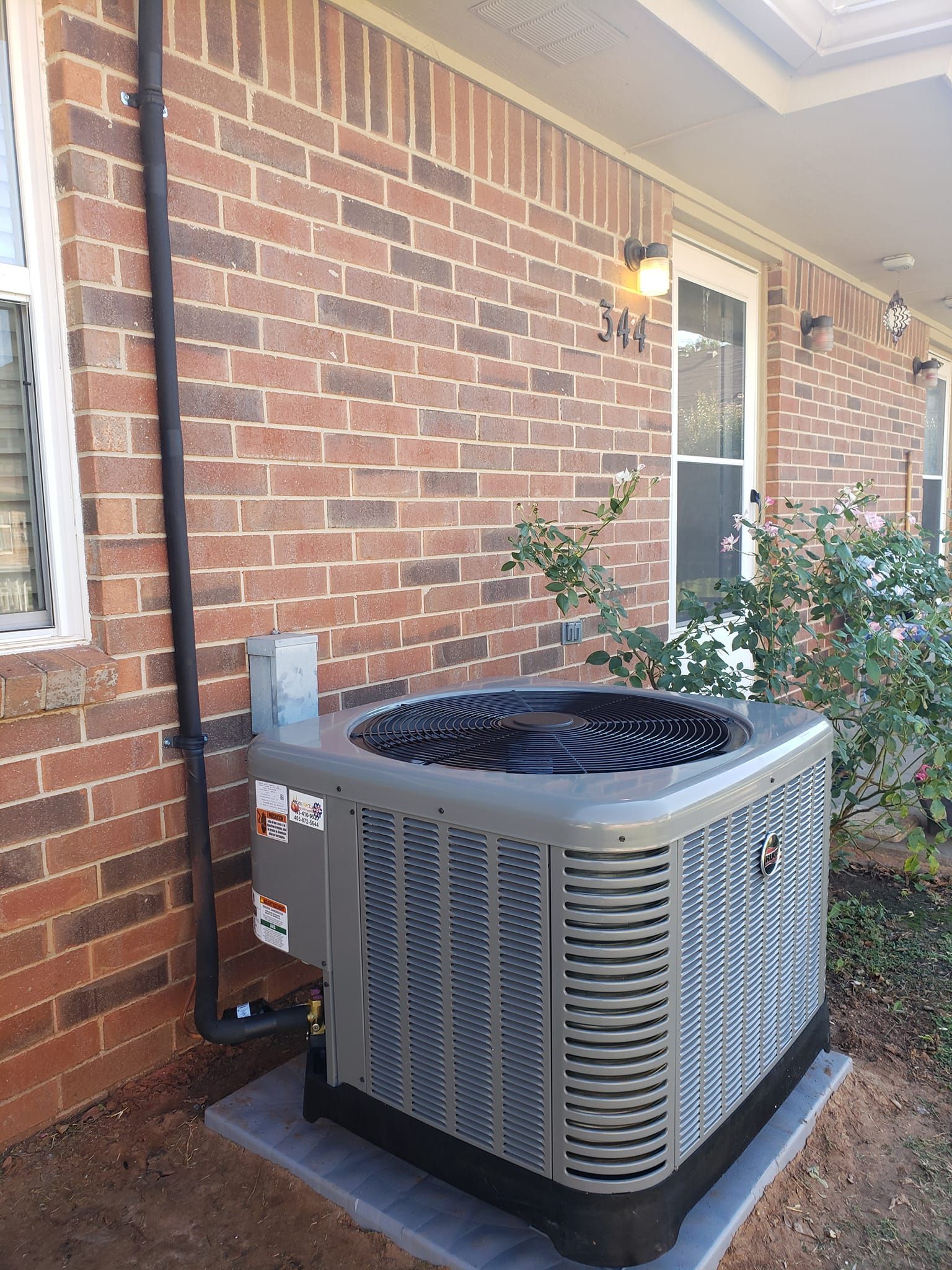 An air conditioner is sitting on the side of a brick house.