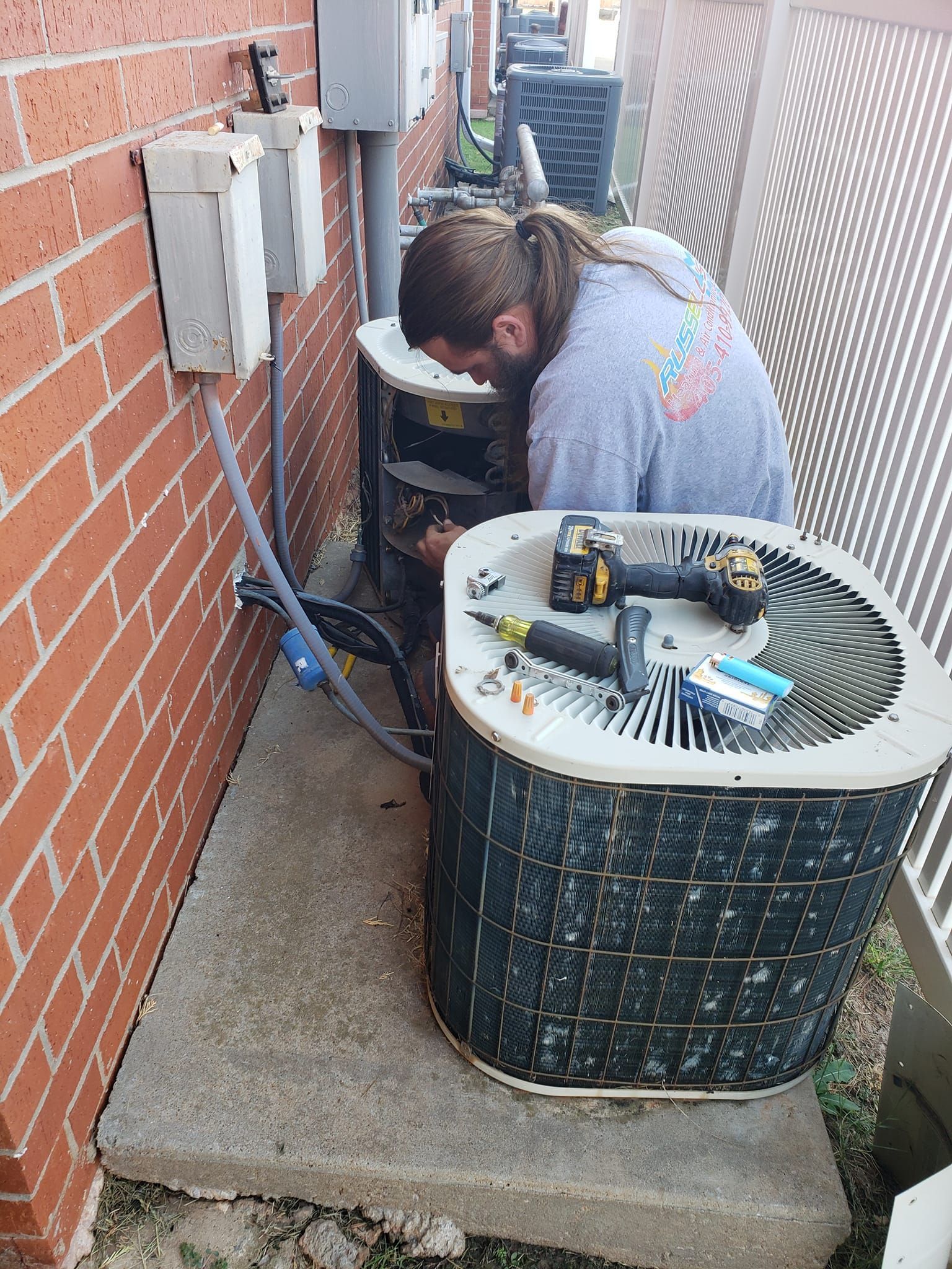 A man is working on an air conditioner outside of a brick building.