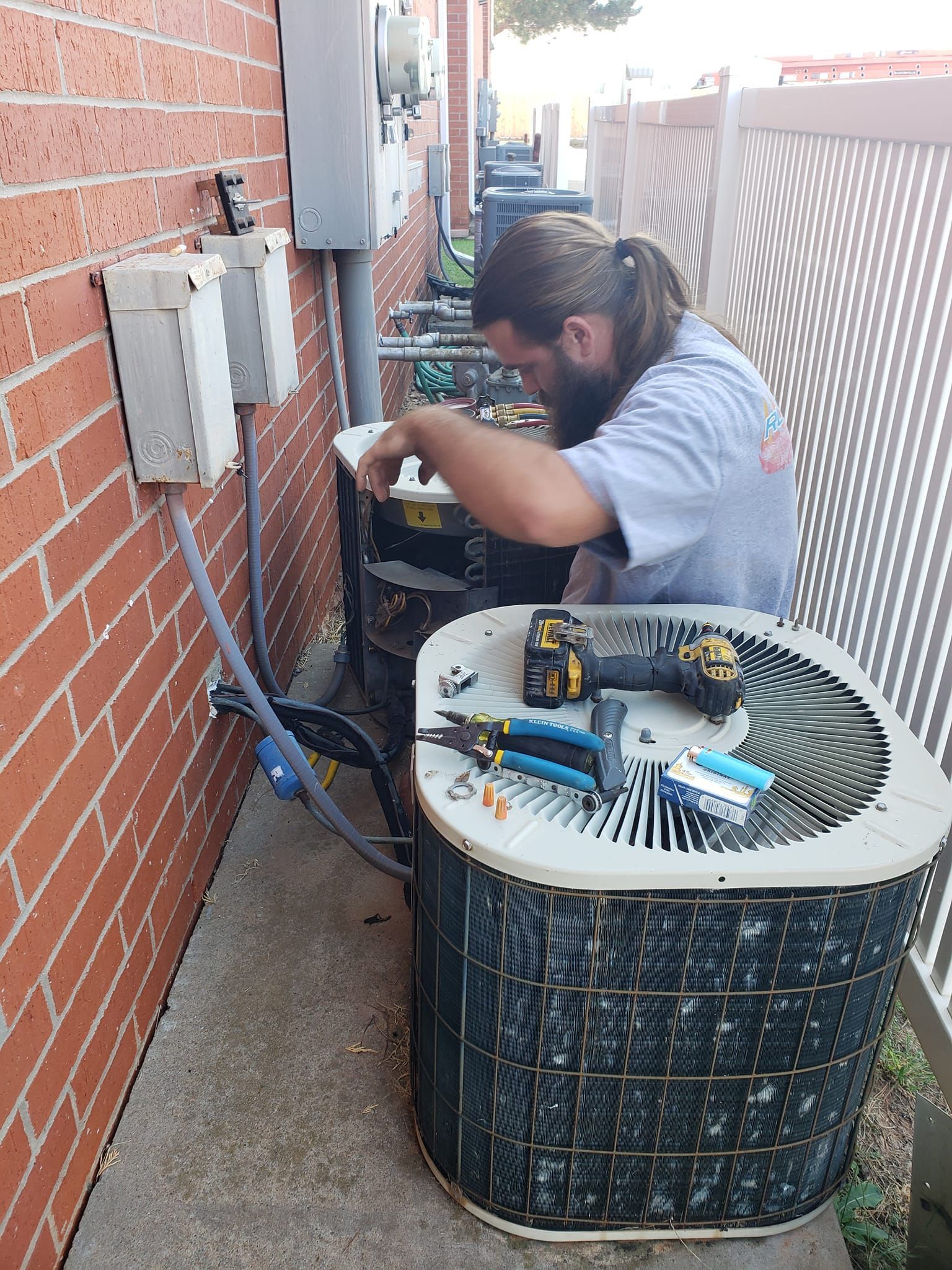 A man is working on an air conditioner outside of a brick building.