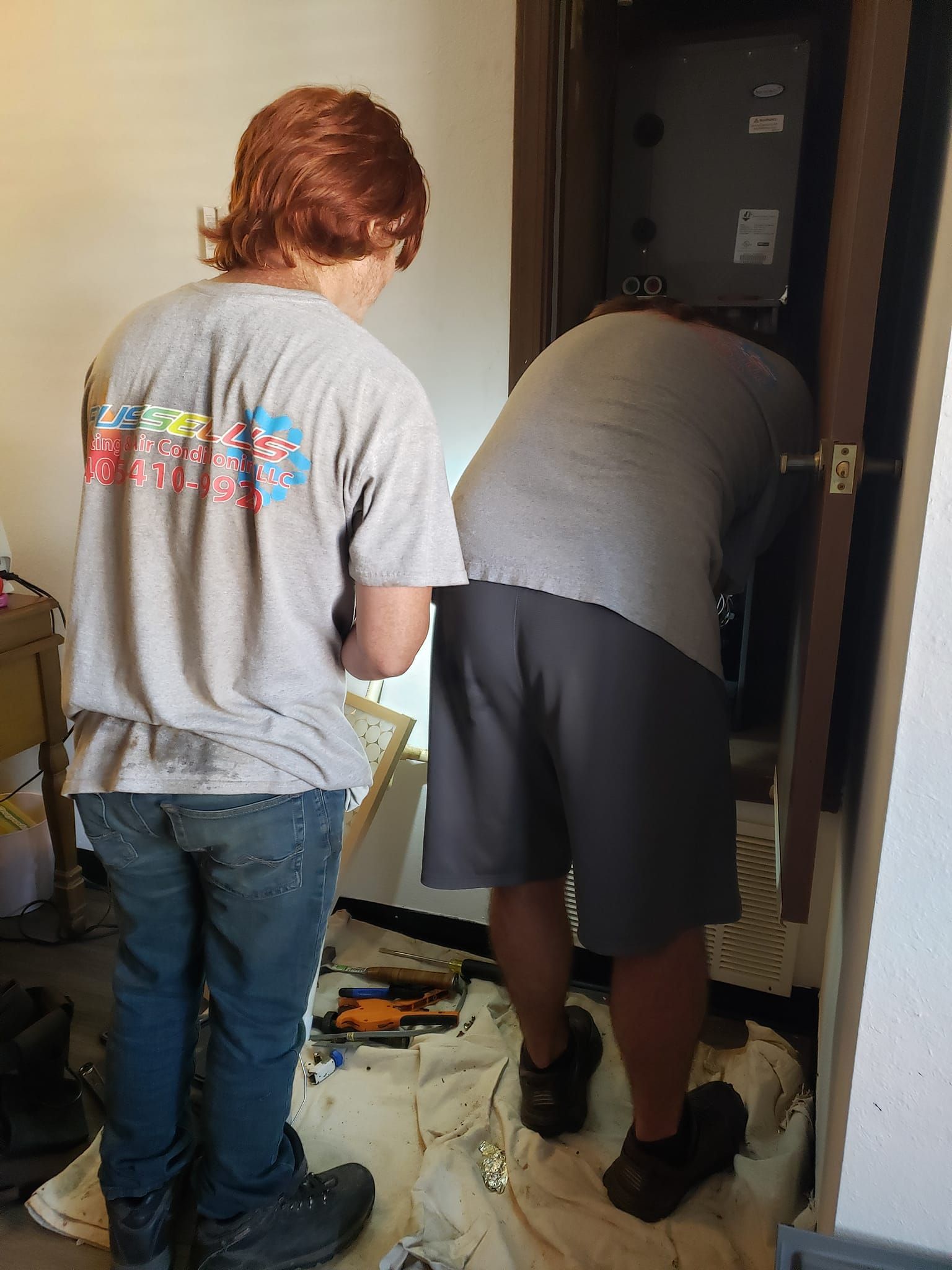 Two men are working on an air conditioner in a room.