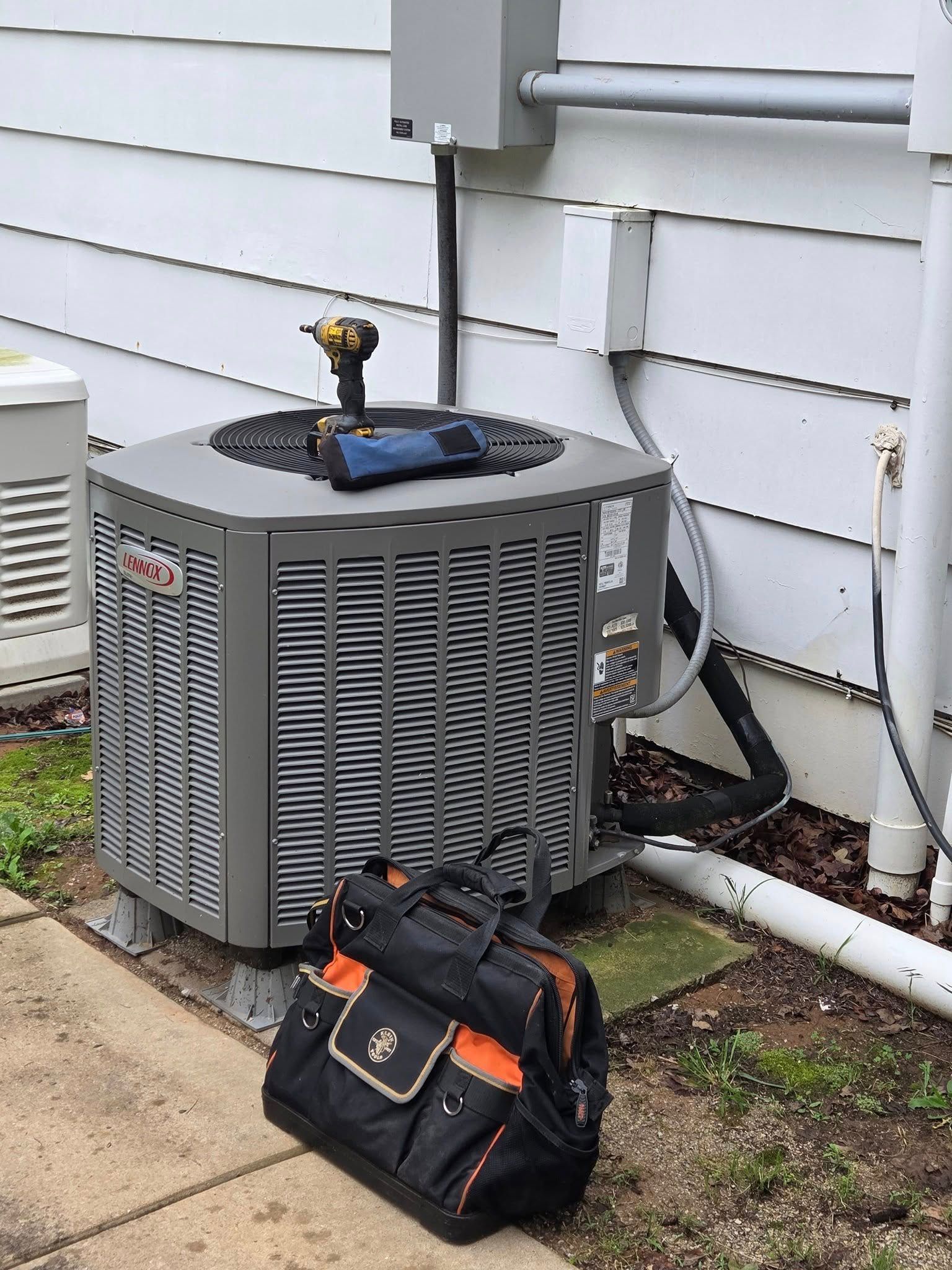 An air conditioner is sitting on the side of a house next to a tool bag.