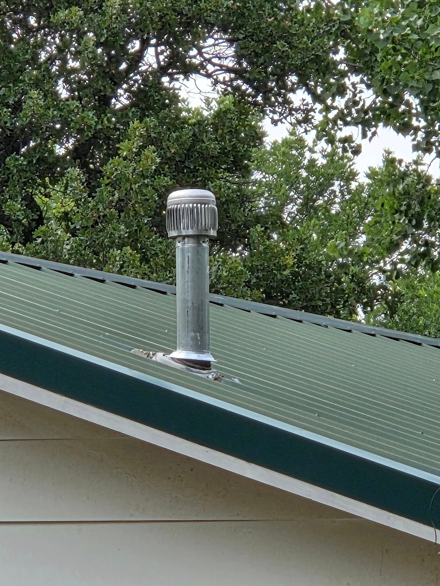 A chimney on the roof of a house with trees in the background.