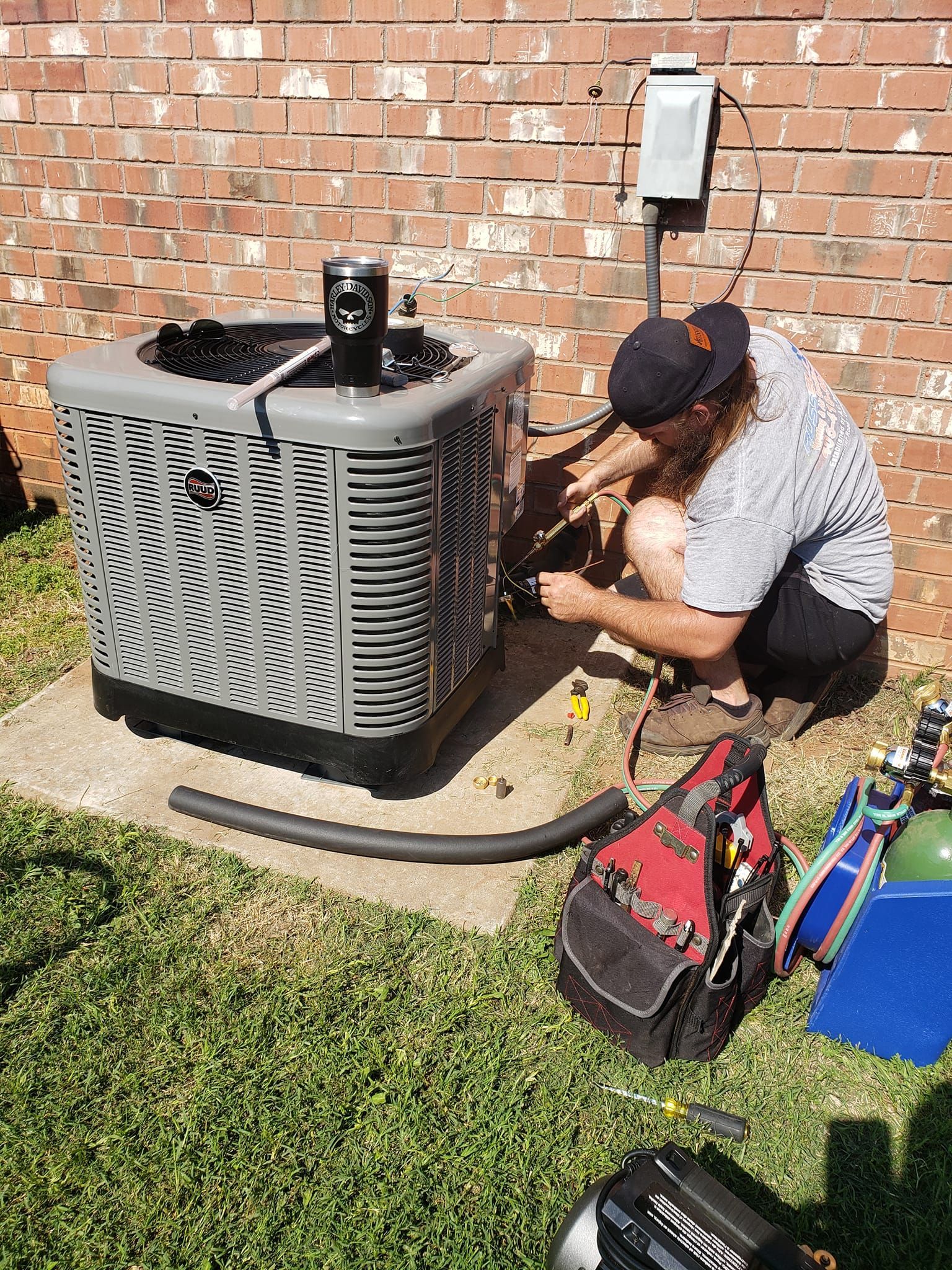 A man is working on an air conditioner outside of a brick building.