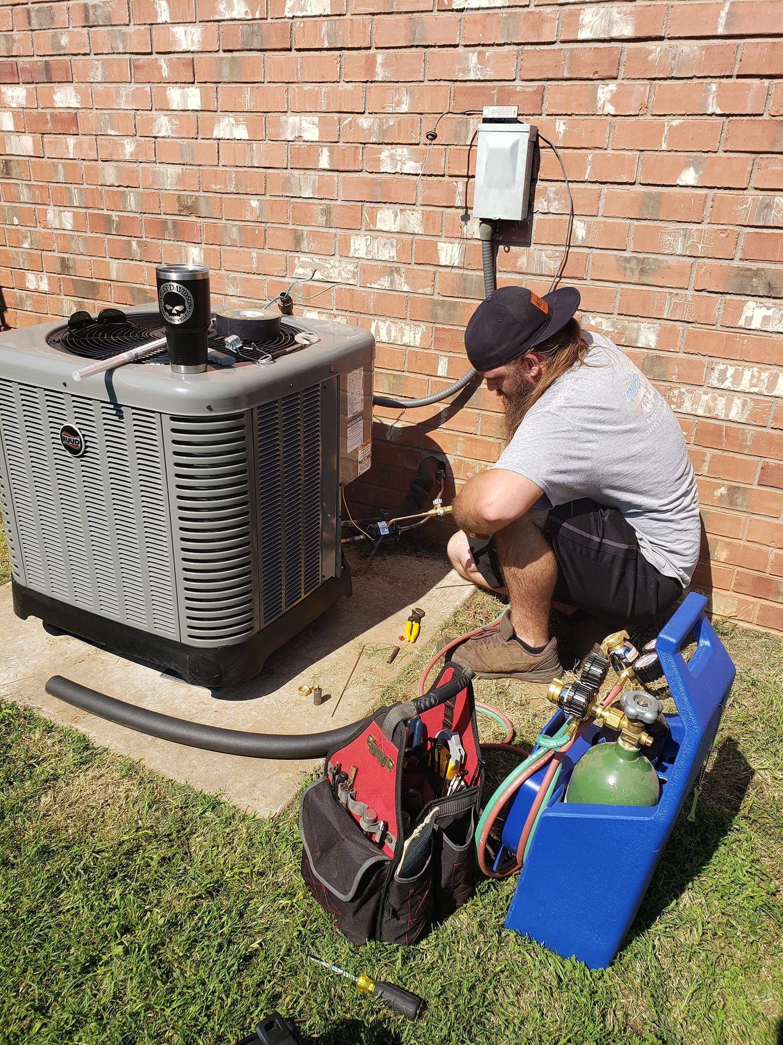 A man is sitting on the ground working on an air conditioner.
