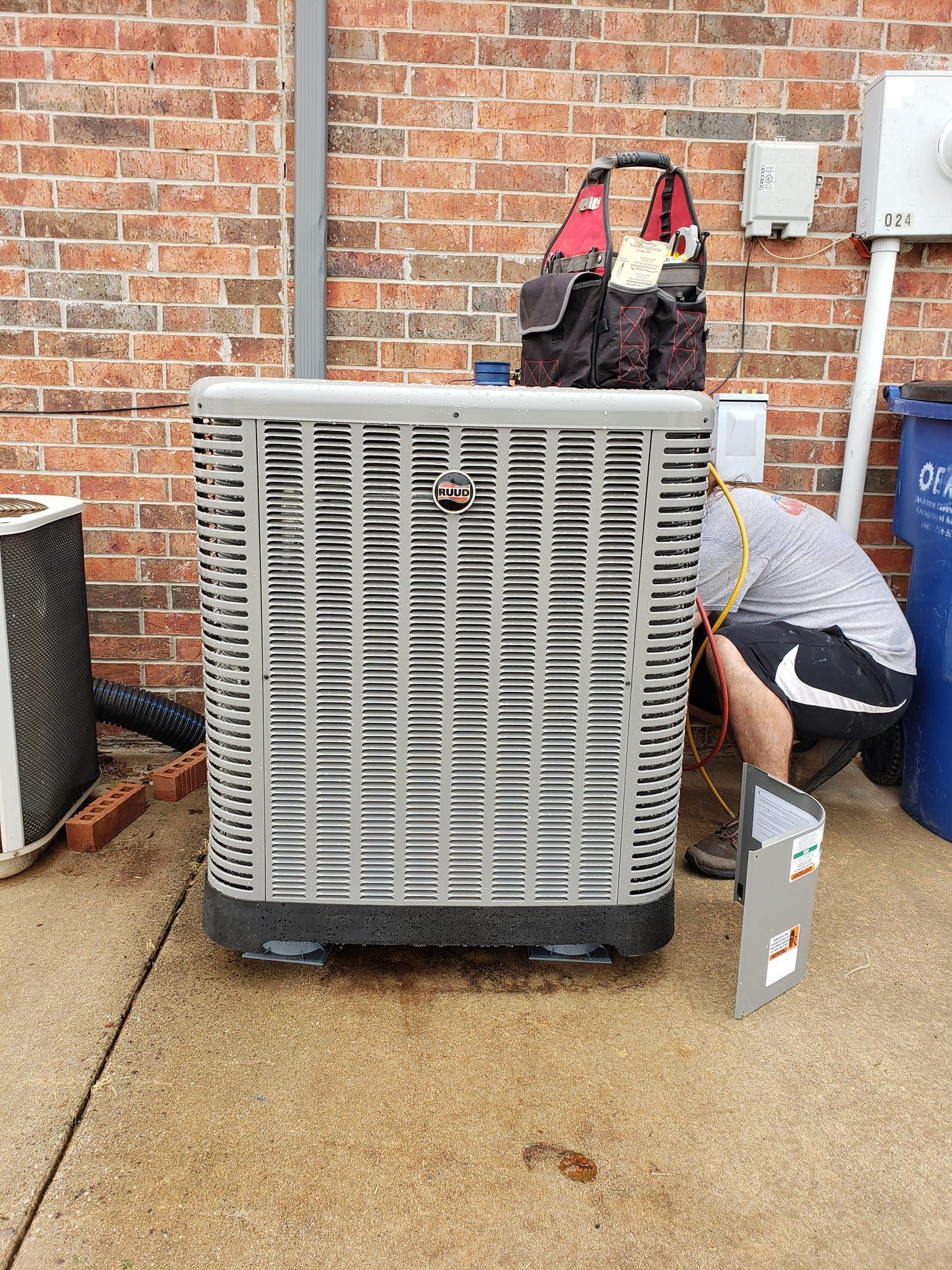 A man is working on an air conditioner outside of a brick building.
