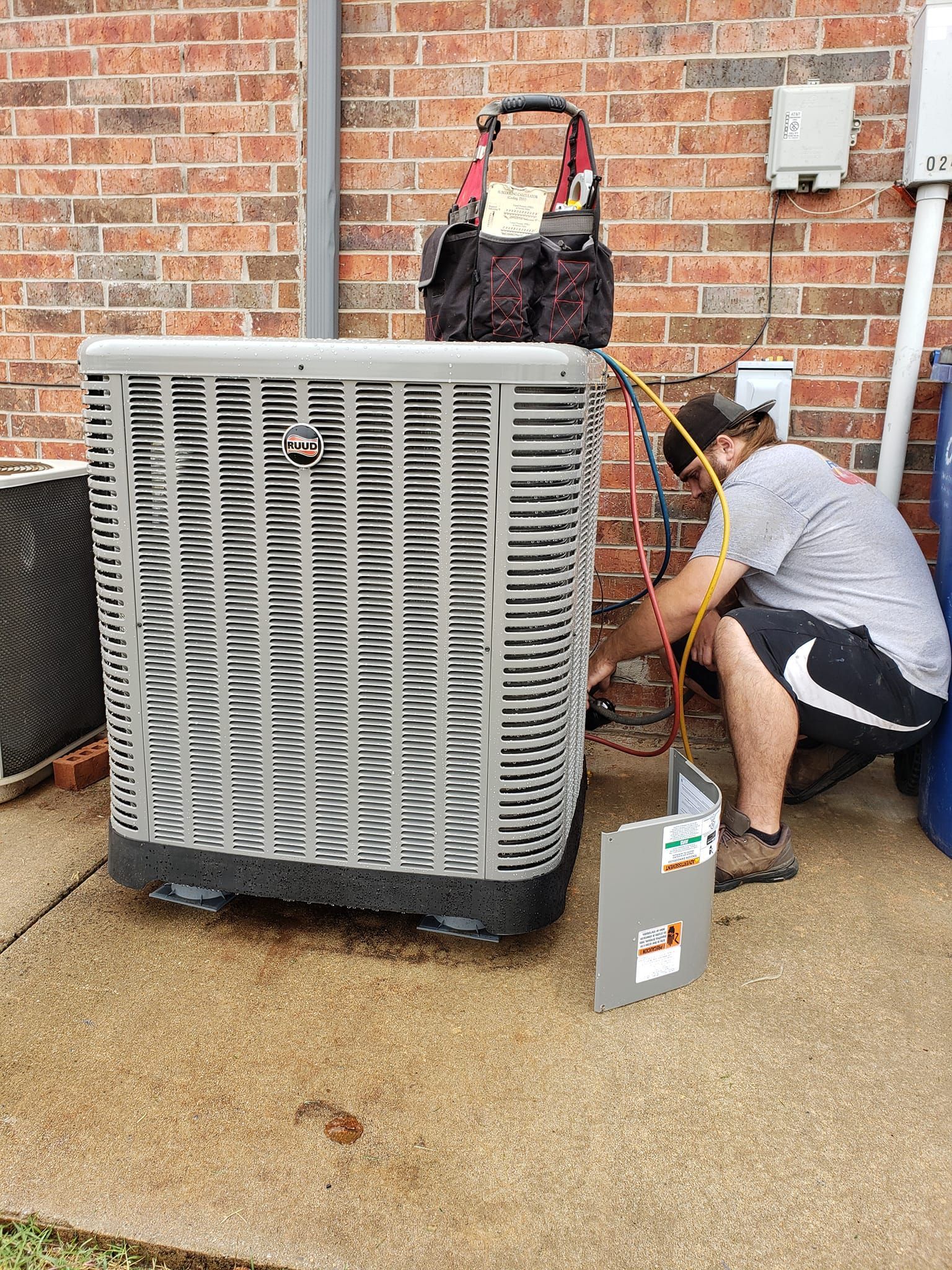 A man is working on an air conditioner outside of a brick building.