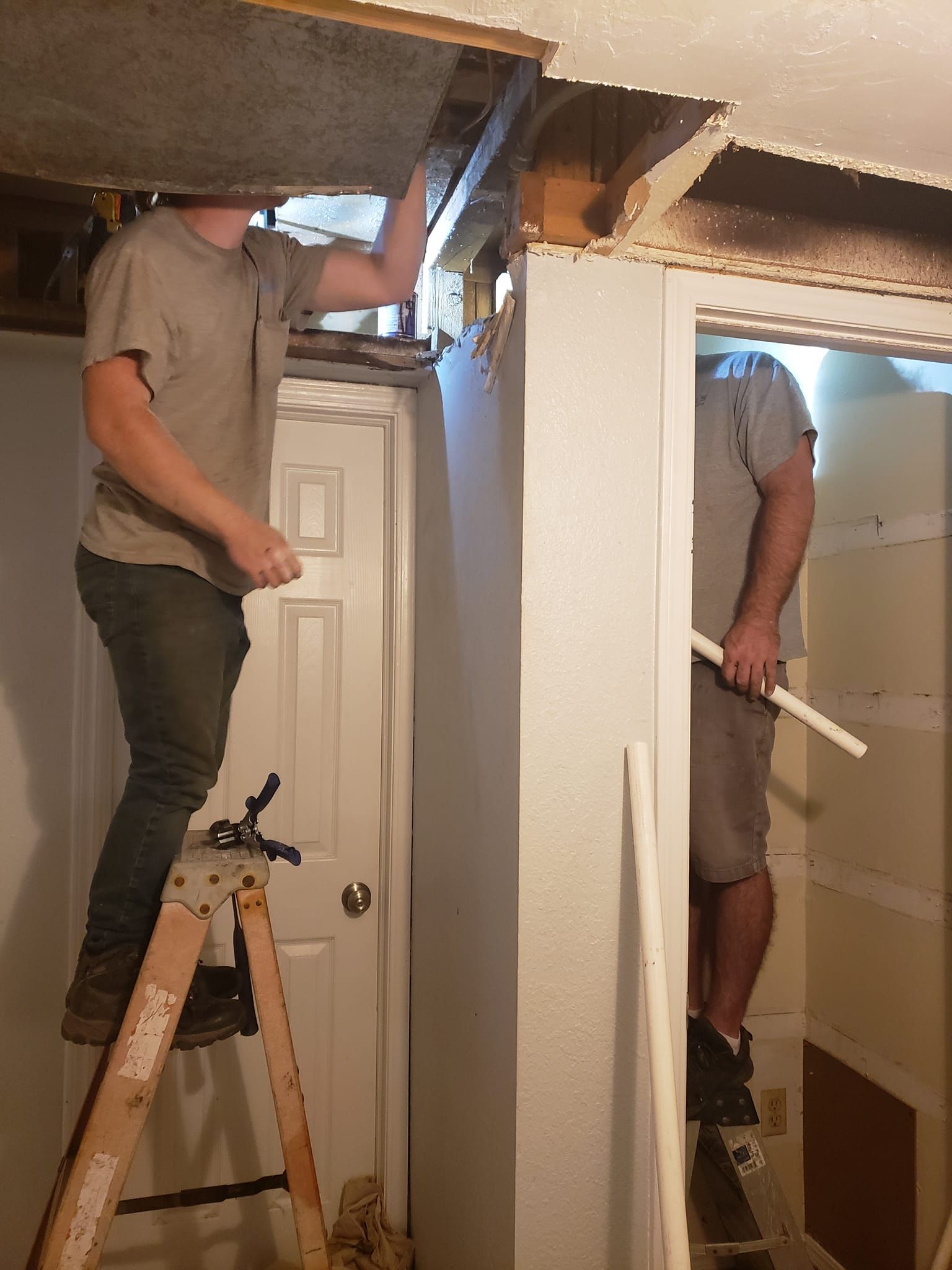 Two men are working on a ceiling in a basement.