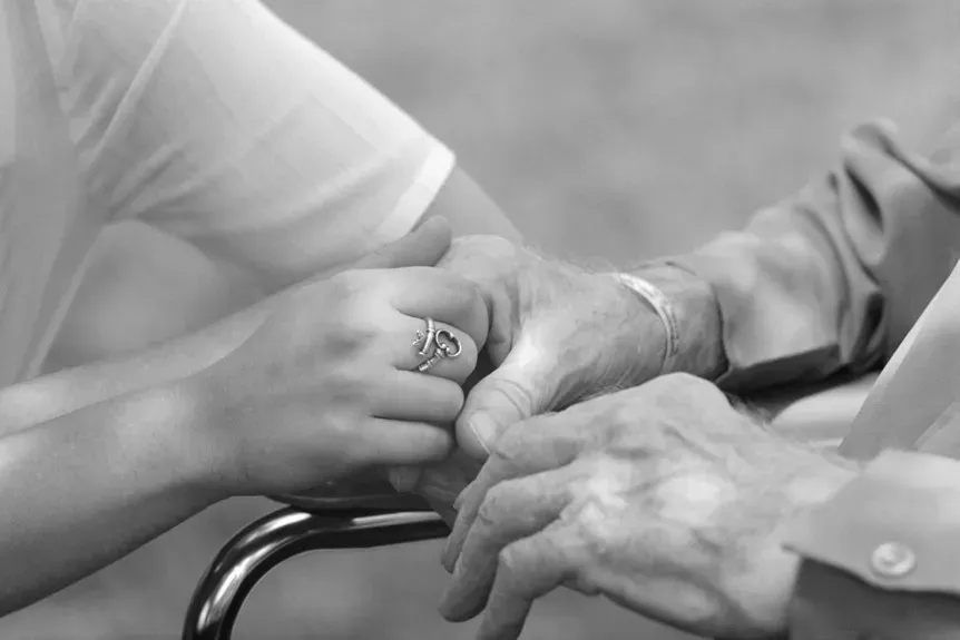 A woman is holding the hand of an elderly woman in a black and white photo.