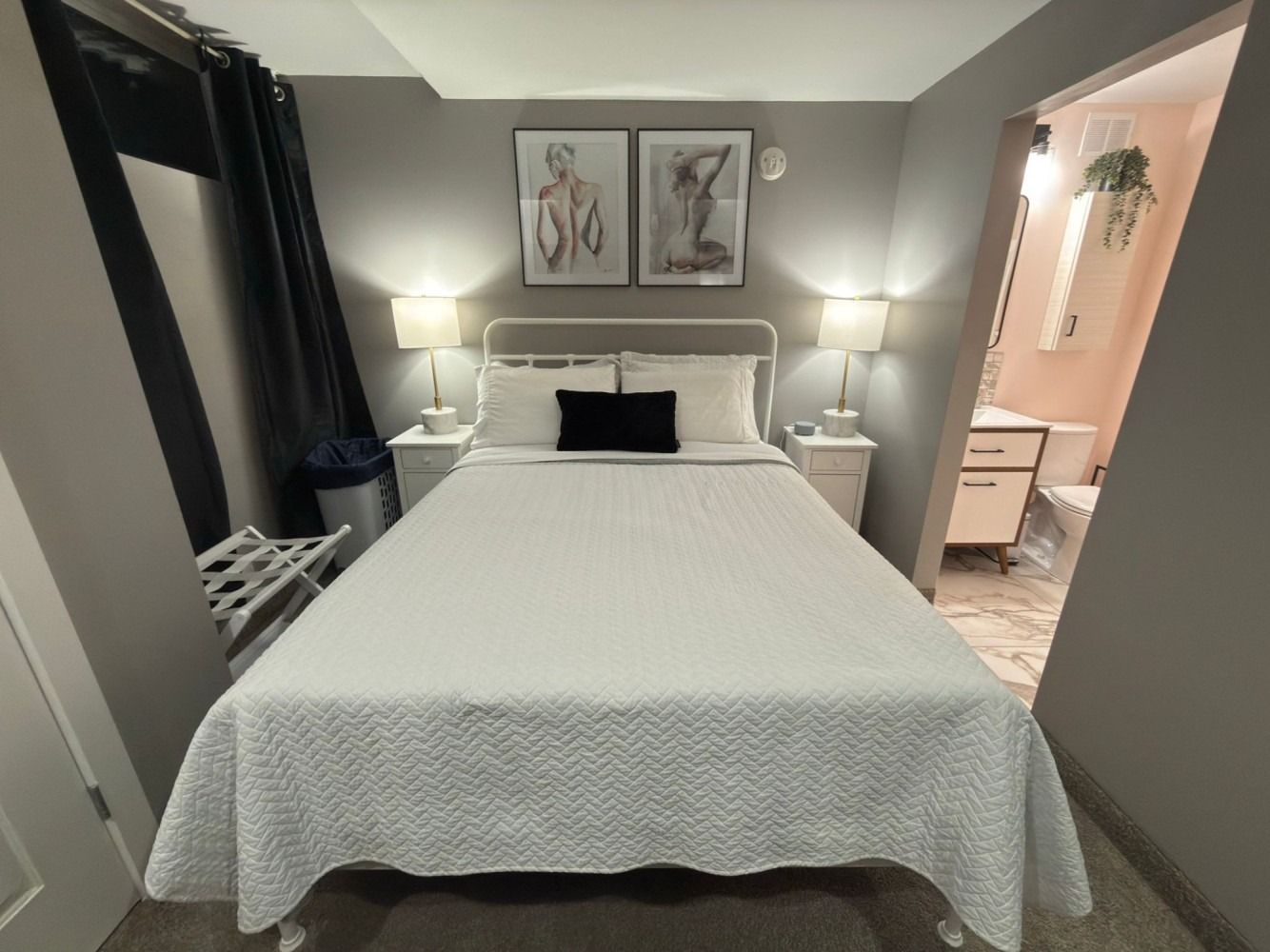 Cozy bedroom with a wooden bed, beige bedding, lamps, wall art, mirror, and warm overhead light.