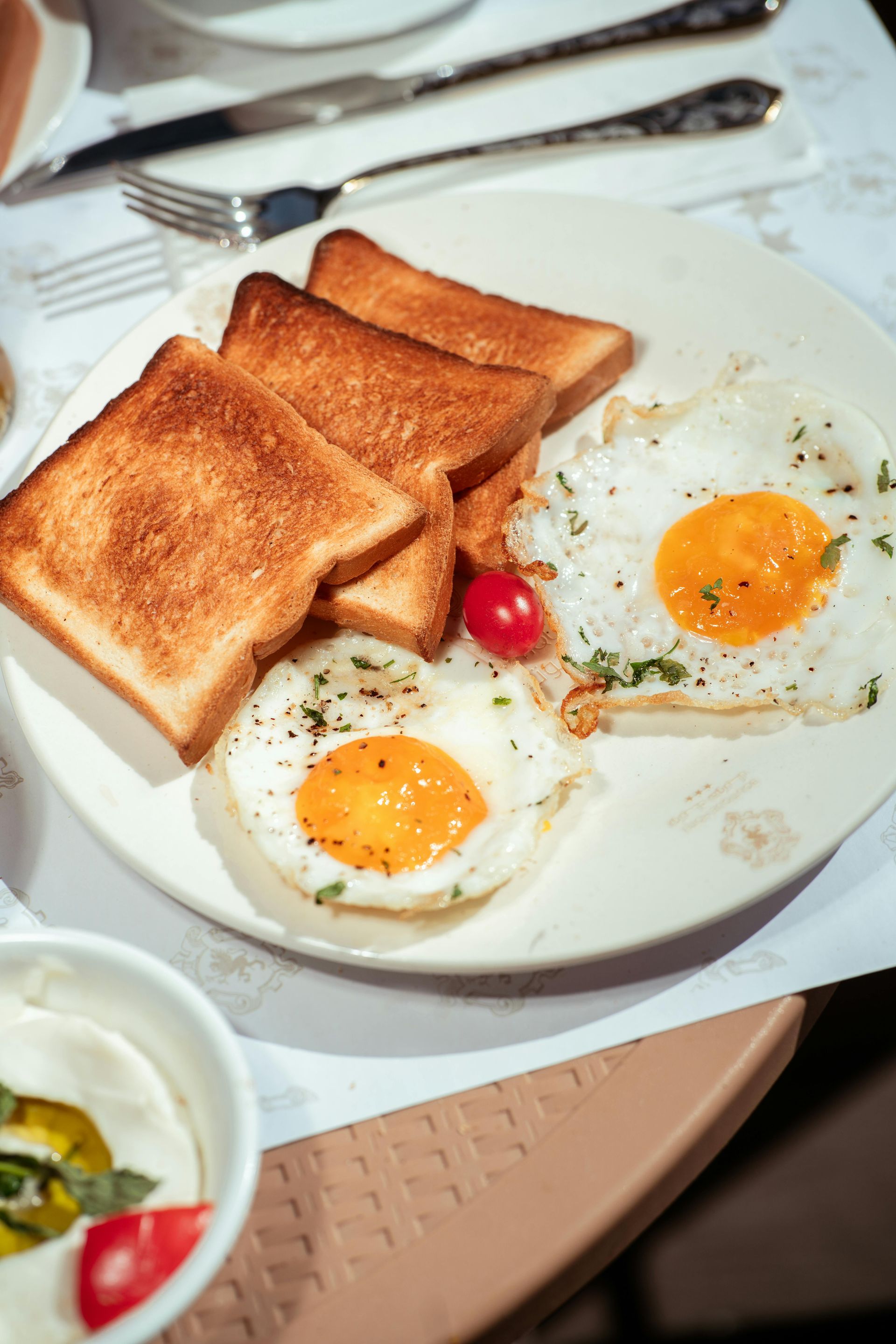 Breakfast plate with toast and two fried eggs, lightly seasoned, on a white table