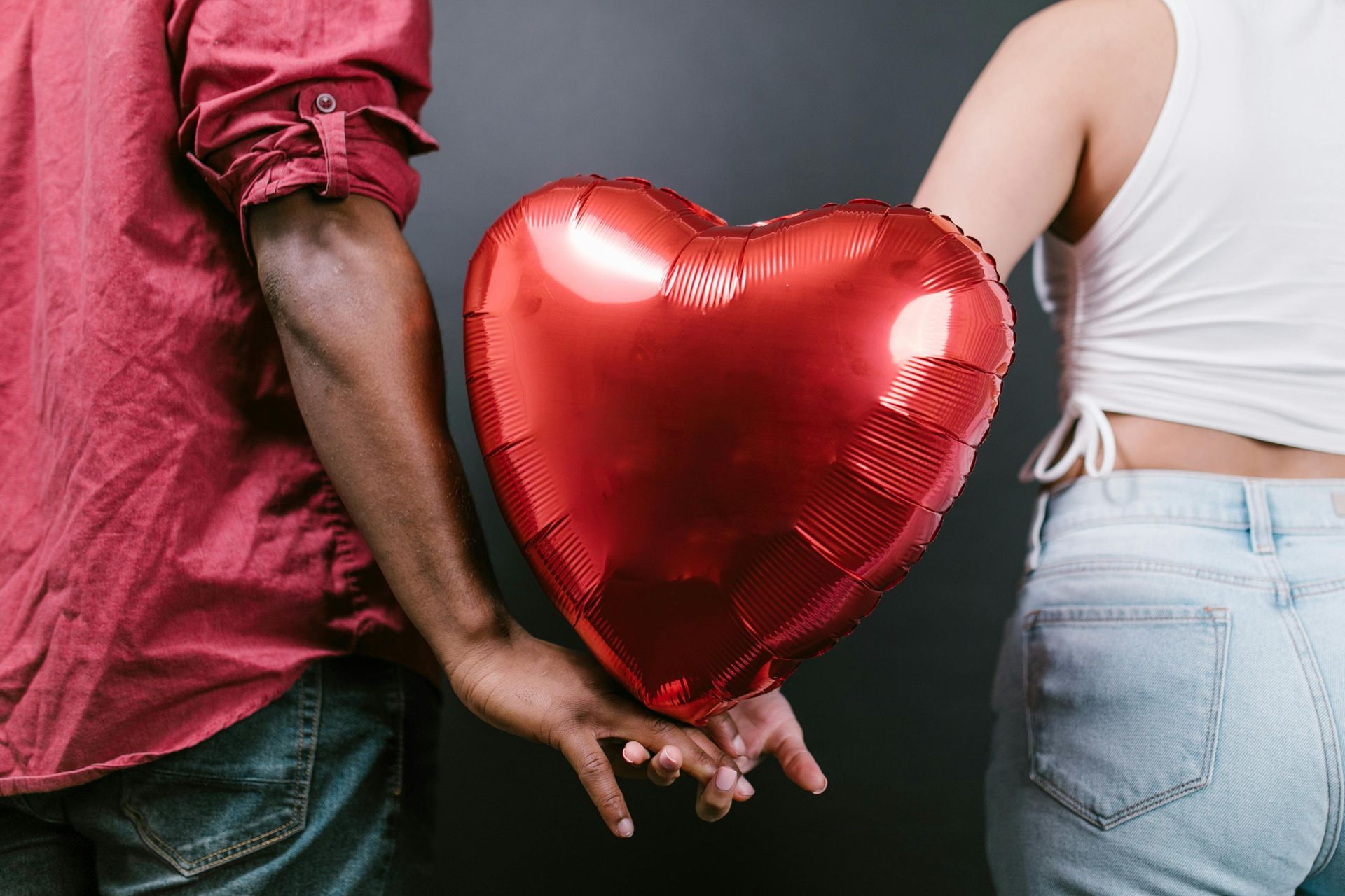 Two people holding a red heart-shaped balloon behind their backs