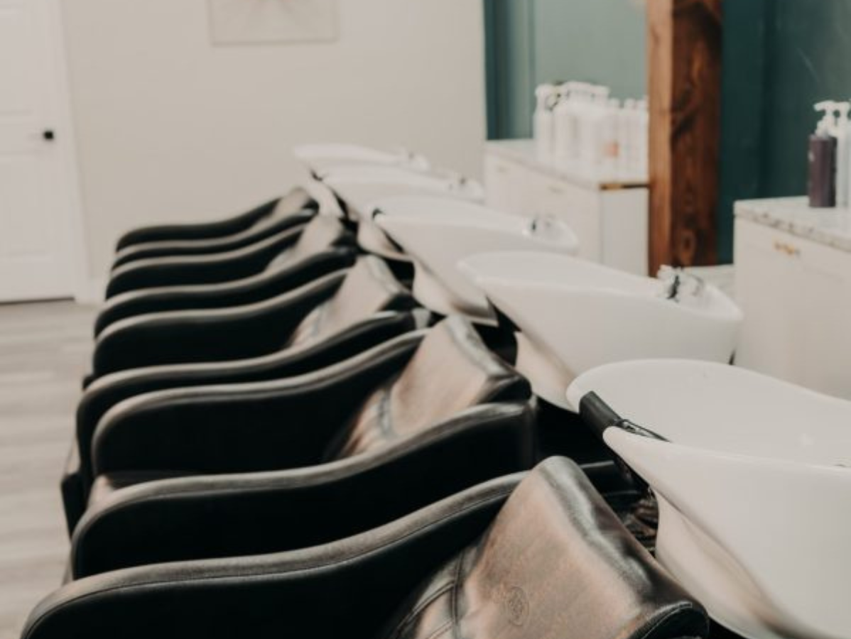 A row of black salon shampoo chairs and white sinks in a bright, modern hair salon.