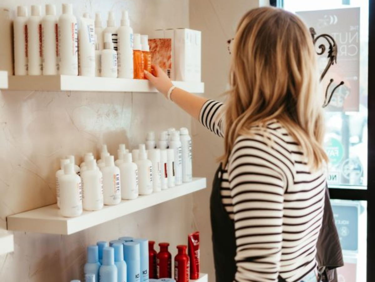 A person in a striped shirt reaching for a bottle of hair product on a white display shelf in a salon.