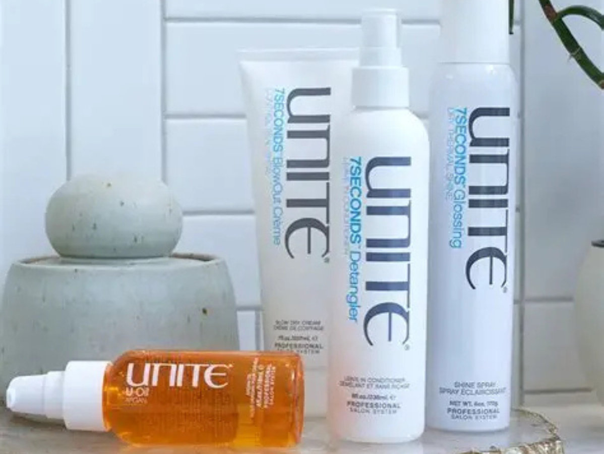 Four bottles of Unite hair care products arranged on a surface against a white tiled background.
