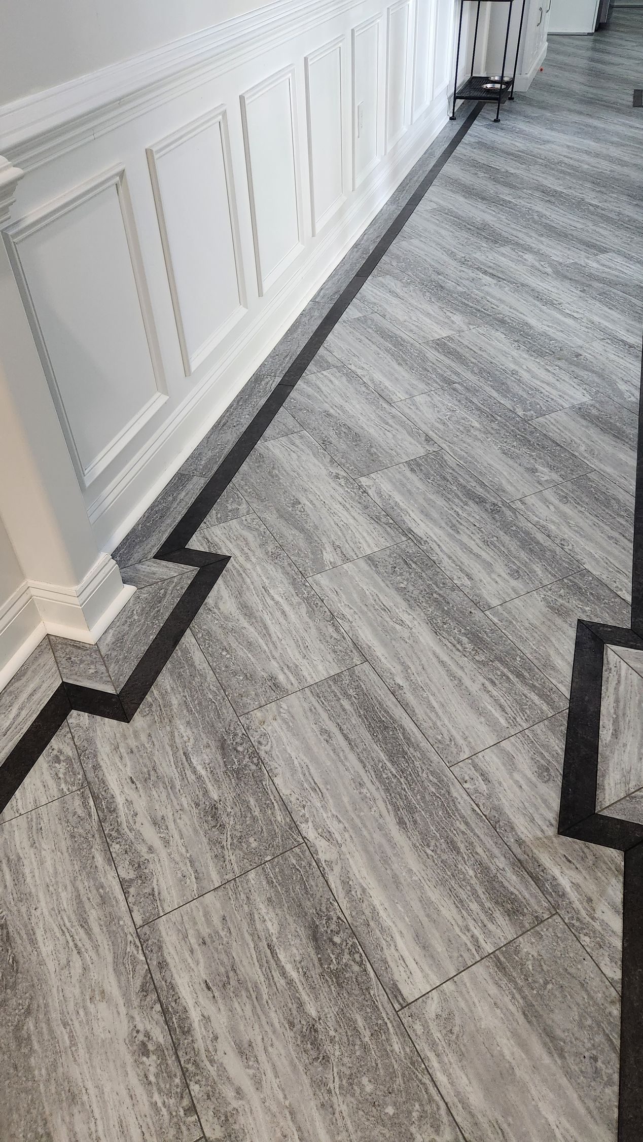 Gray carpeted hallway with white paneled walls and dark trim along the edges