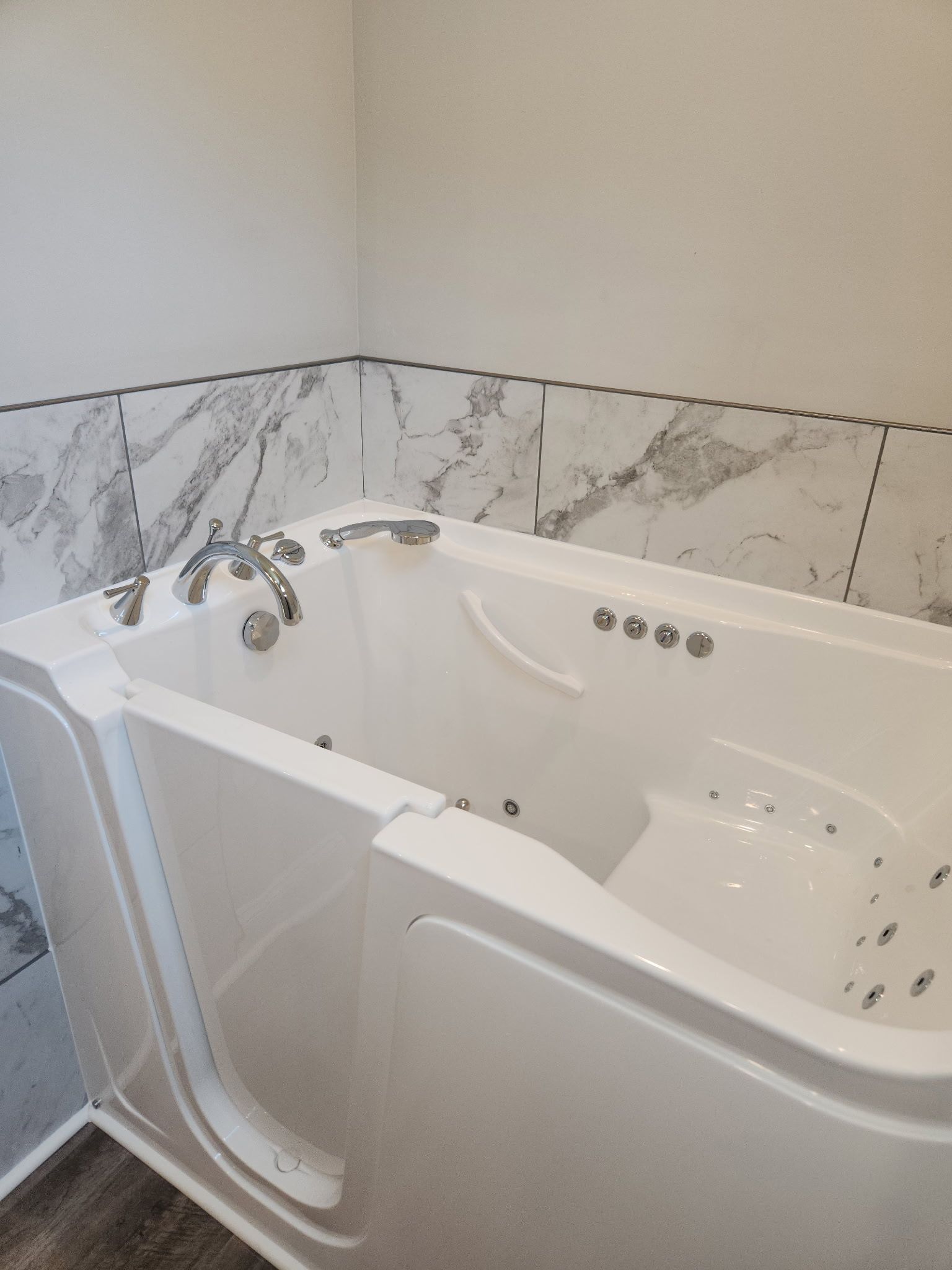 White walk-in bathtub with grab bar and marble-look tile walls in a bathroom.