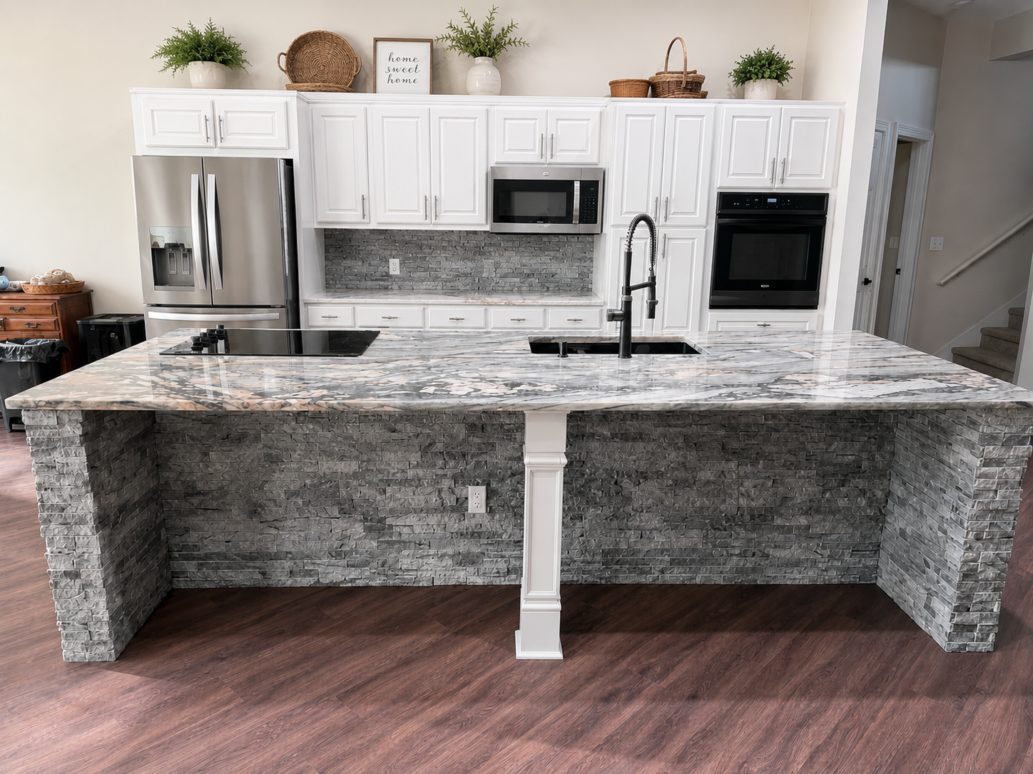 Modern kitchen with a large stone island, stainless steel appliances, white cabinets, and wood flooring