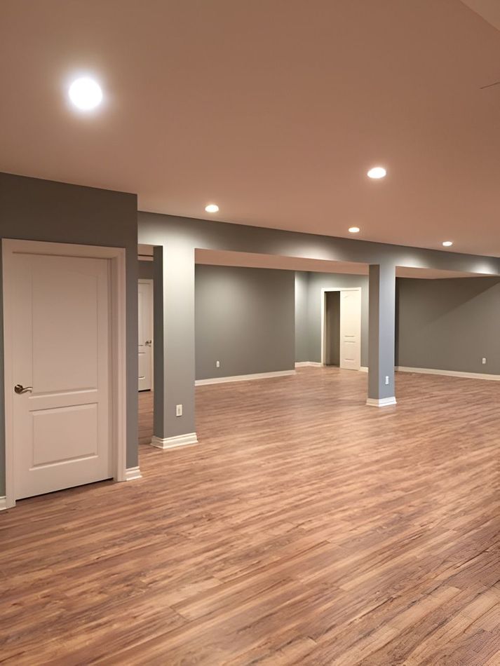 Empty finished basement with wood-look flooring, gray walls, white columns, and recessed ceiling lights.
