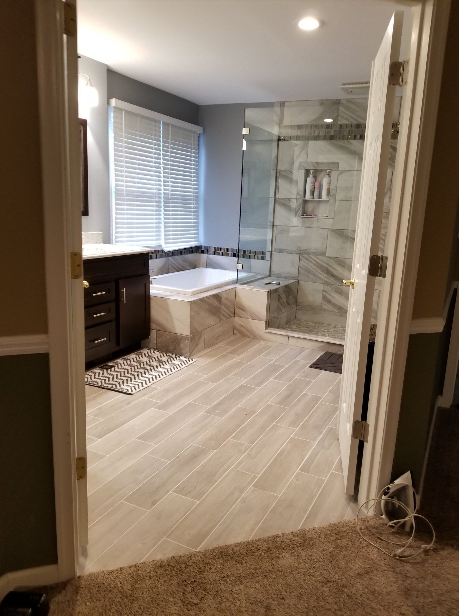 Bathroom with tiled floor, vanity, tub, and glass shower enclosure, viewed from the doorway.