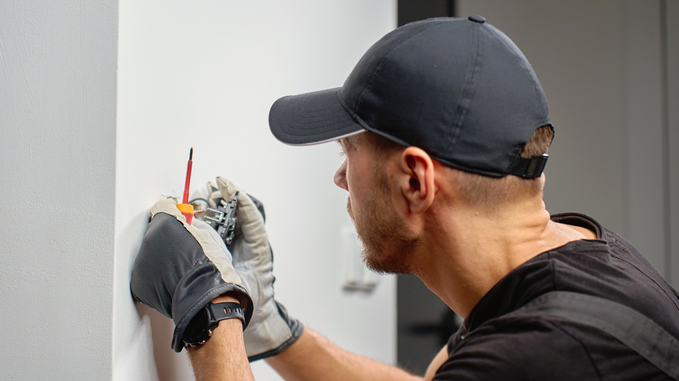 Technician in gloves uses a tool to work on a wall fixture near a white surface.