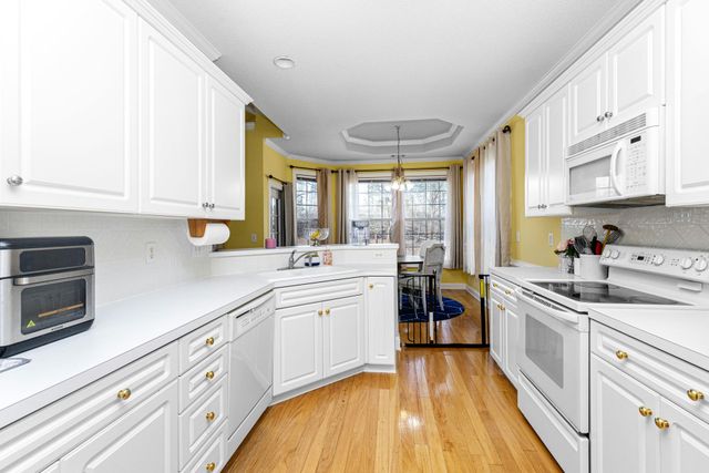 Bright white kitchen with stainless appliances, wood floor, yellow walls, and a dining area beyond the counter.