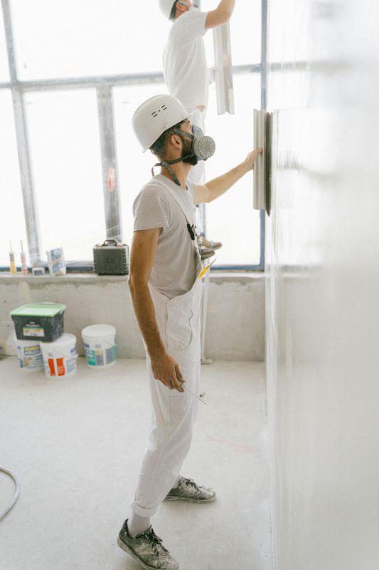 Two painters in white overalls painting a bright room with a large window