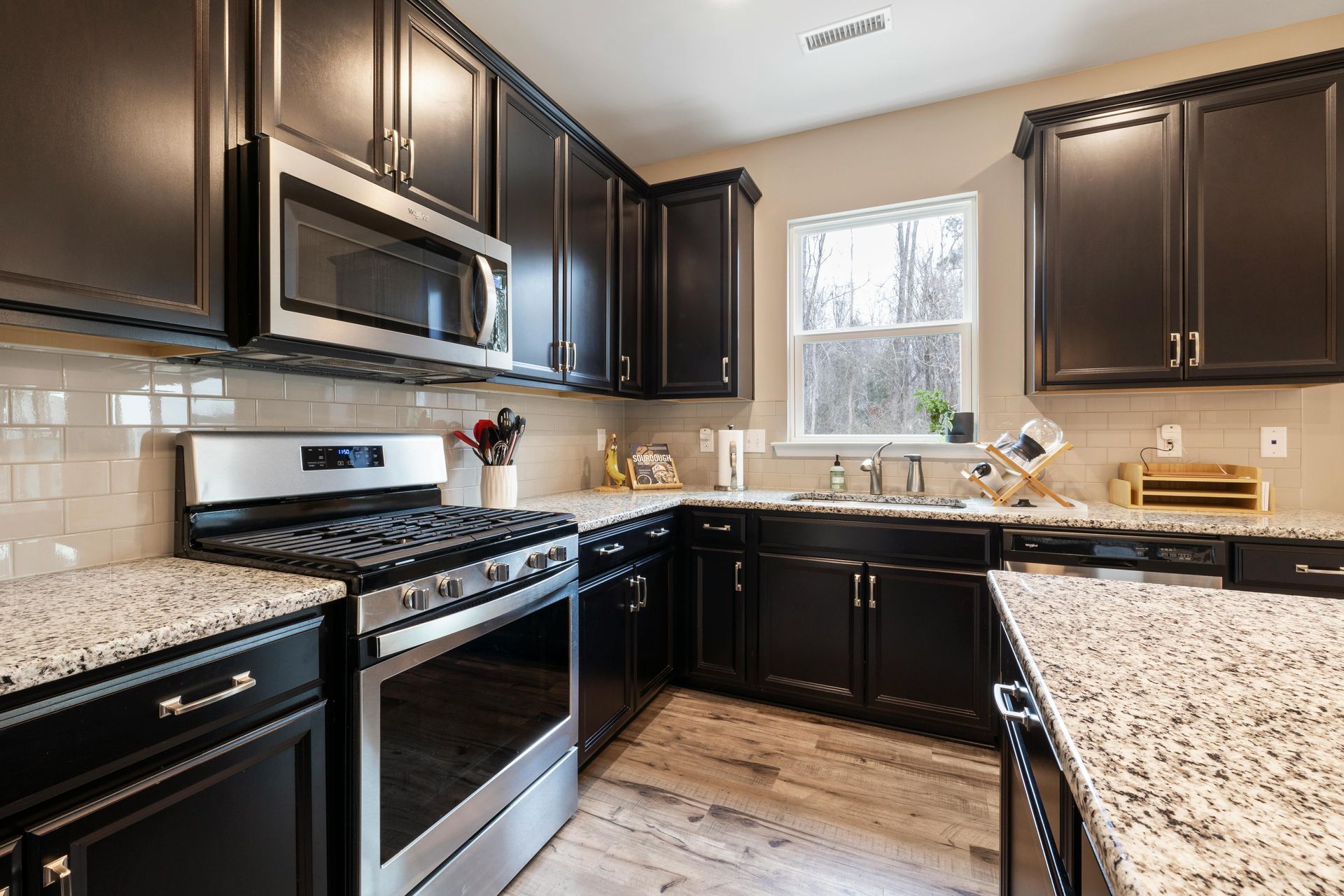 Modern kitchen with dark cabinets, stainless steel appliances, white backsplash, and a window over the sink