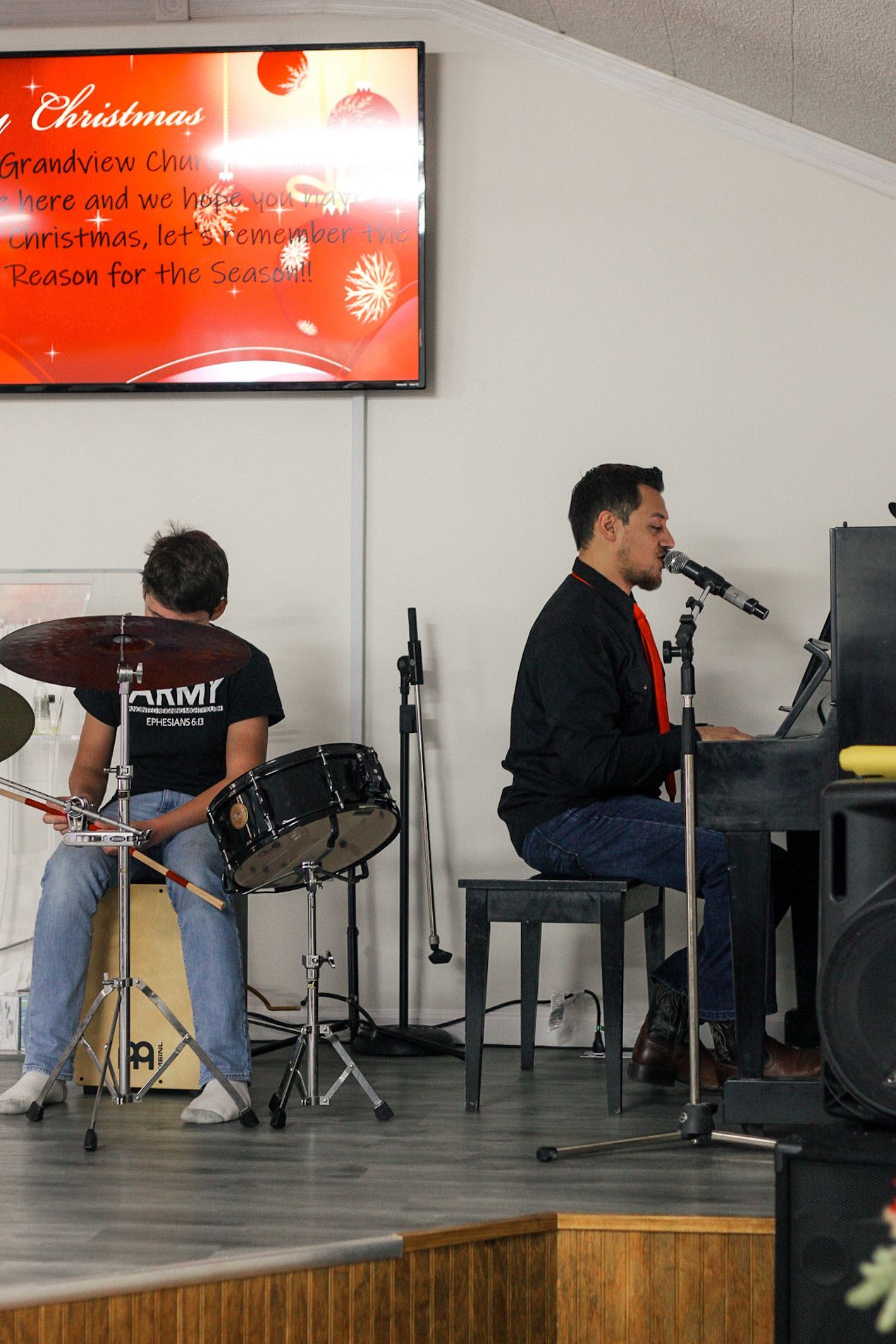 A man is playing drums and another man is playing a piano.