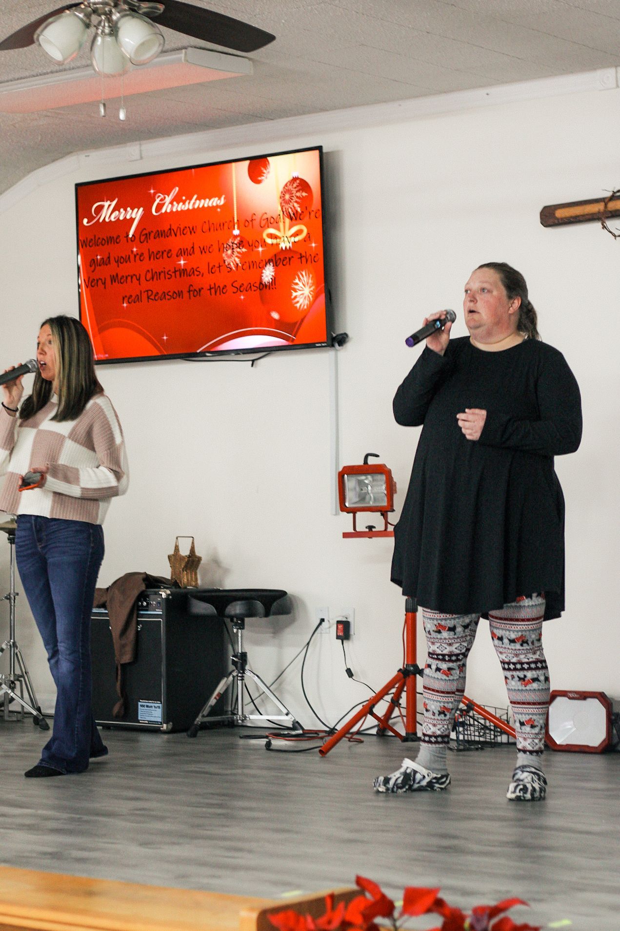 Two women singing in front of a screen that says merry christmas