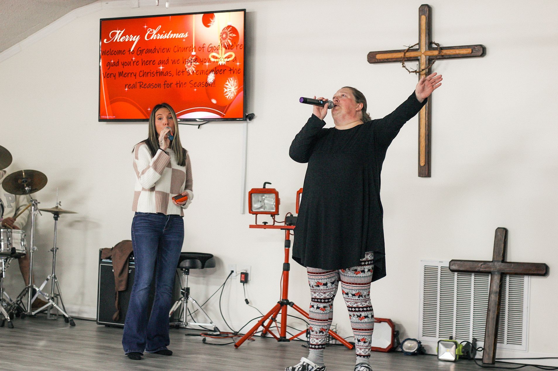 Two women are singing into microphones in front of a cross.